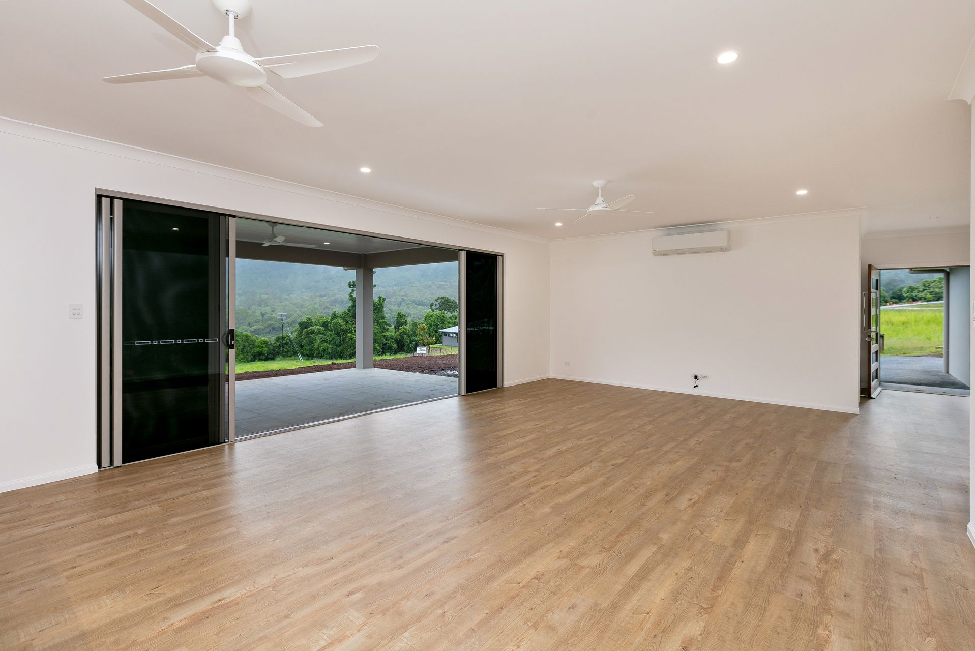 A Modern, Spacious Living Area With Light Wood Floors, a Ceiling Fan — Ashlee Jones Homes in Gordonvale, QLD