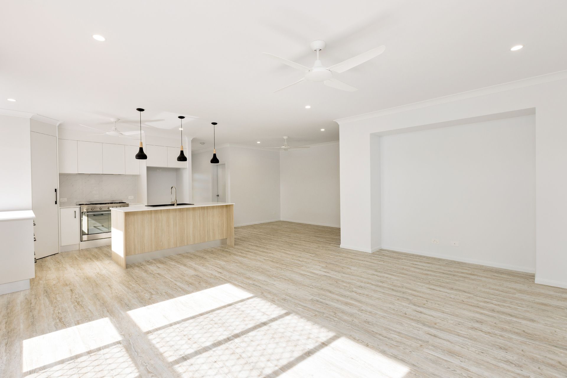 An Open-plan Kitchen and Living Space With White Walls, Light Wood Flooring — Ashlee Jones Homes in Gordonvale, QLD
