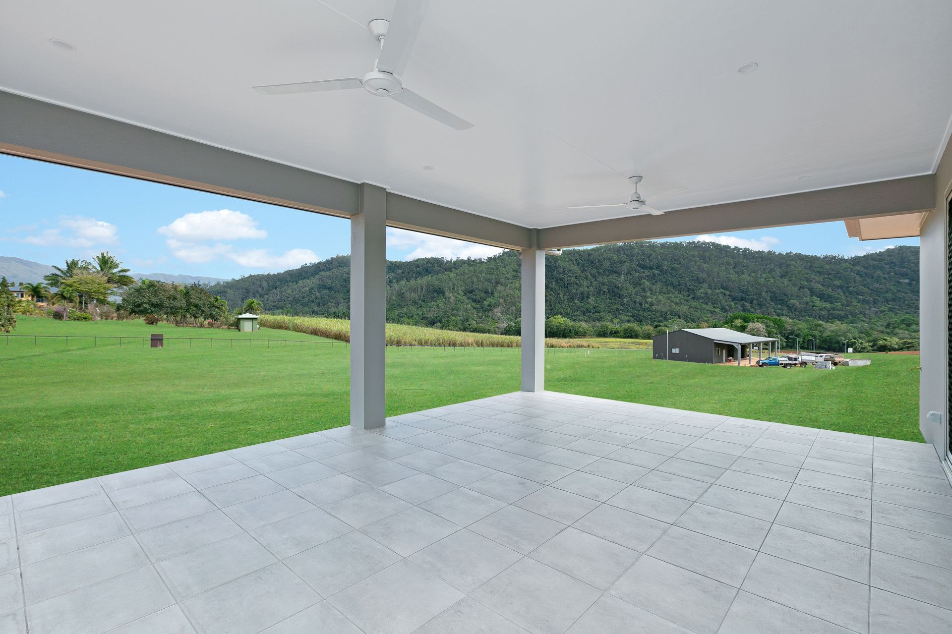 A Spacious Covered Patio With White Tiled Flooring Overlooks — Ashlee Jones Homes in Gordonvale, QLD