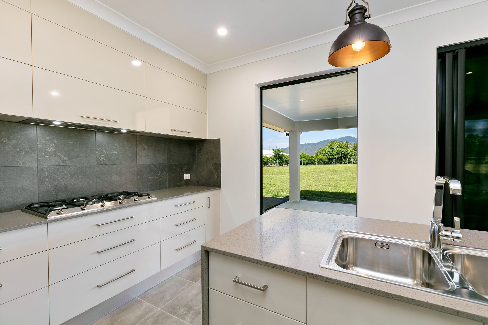 A Modern Kitchen With Cream Cabinets, Grey Backsplash — Ashlee Jones Homes in Gordonvale, QLD