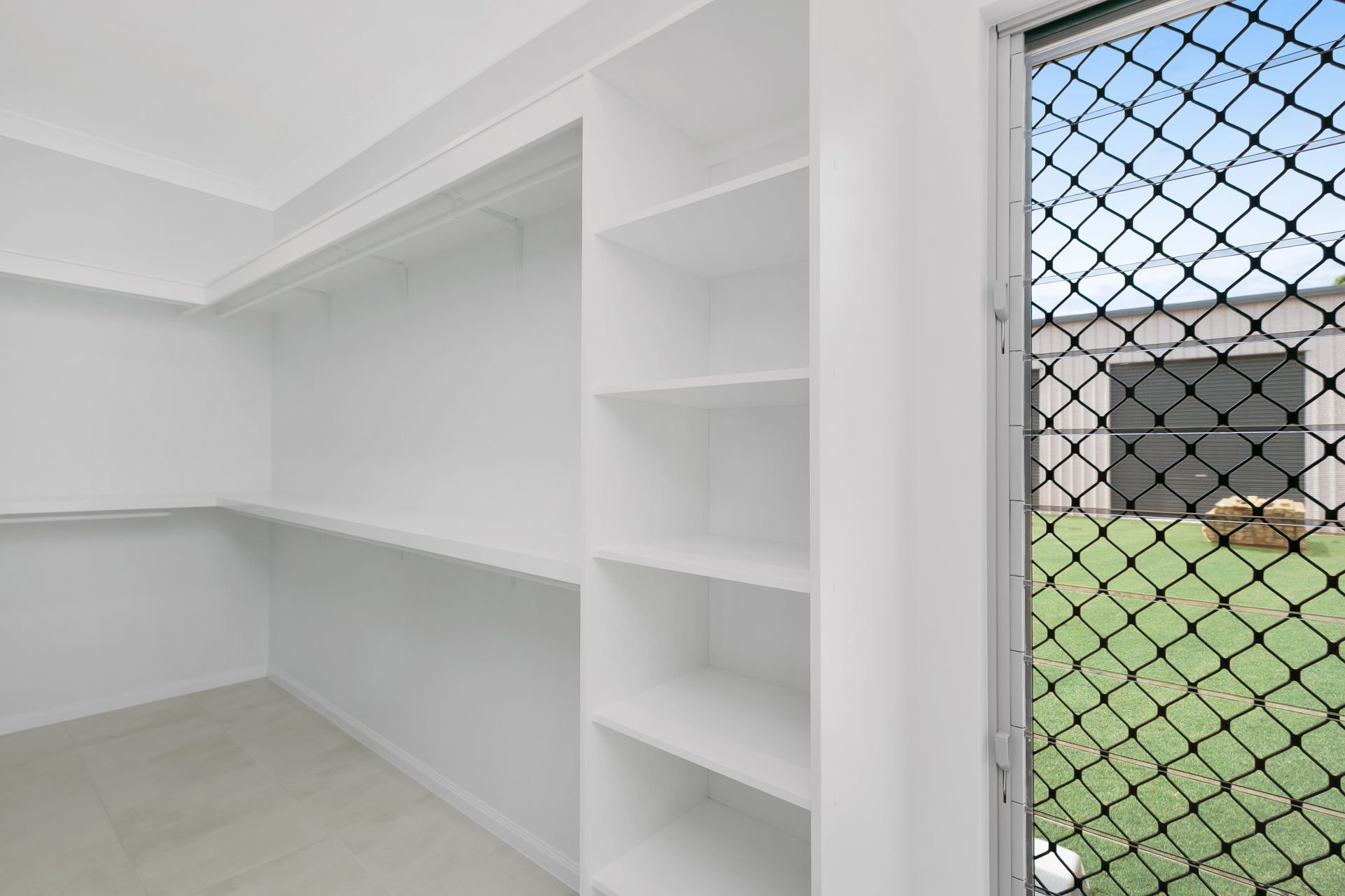 White Interior Walk-in Closet With Shelves and a Screen Door Looking Out — Ashlee Jones Homes in Gordonvale, QLD