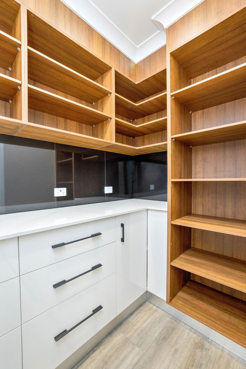 A Modern Walk-in Pantry Featuring White Cabinets With Dark Handles — Ashlee Jones Homes in Gordonvale, QLD