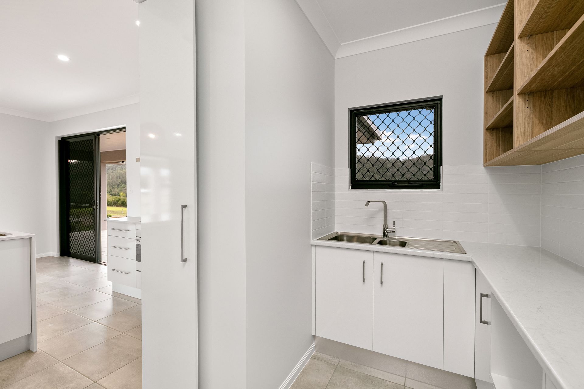 A Bright Laundry Room With White Cabinets, a Sink, Wooden Open Shelving — Ashlee Jones Homes in Gordonvale, QLD