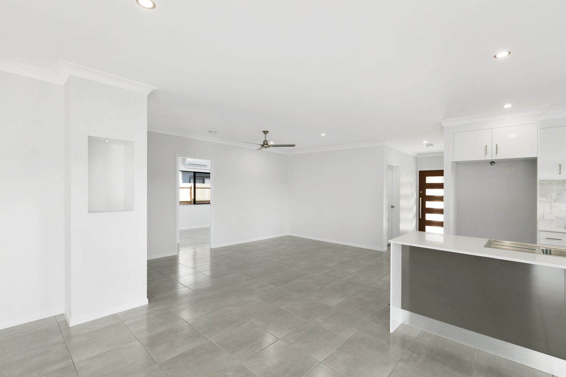 A Bright, Empty Living Area With Grey Tiled Floors, White Walls — Ashlee Jones Homes in Gordonvale, QLD