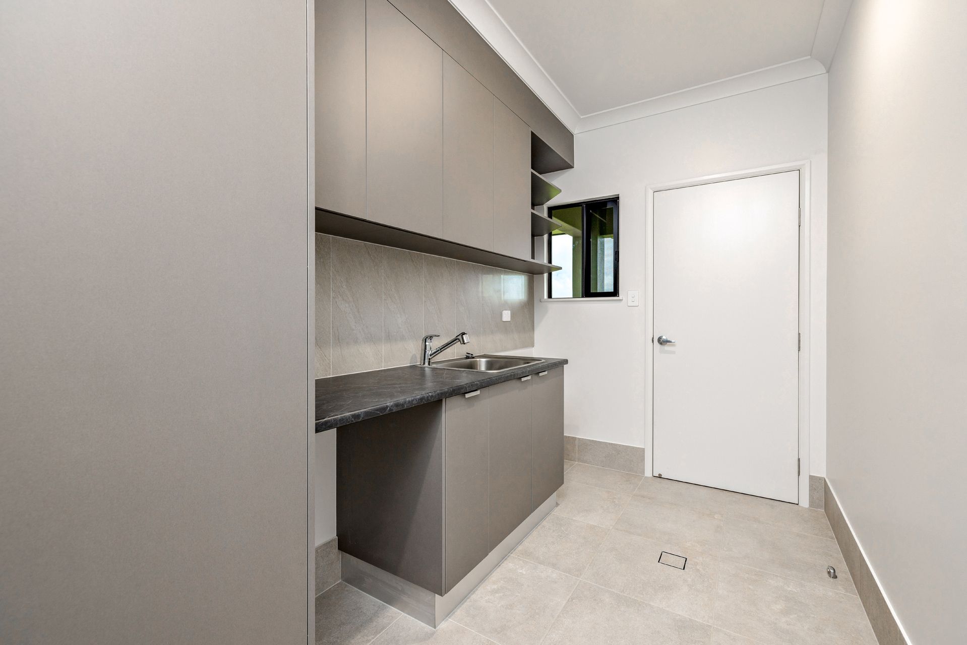 A Laundry Room With Taupe Cabinetry, a Stainless Steel Sink — Ashlee Jones Homes in Gordonvale, QLD