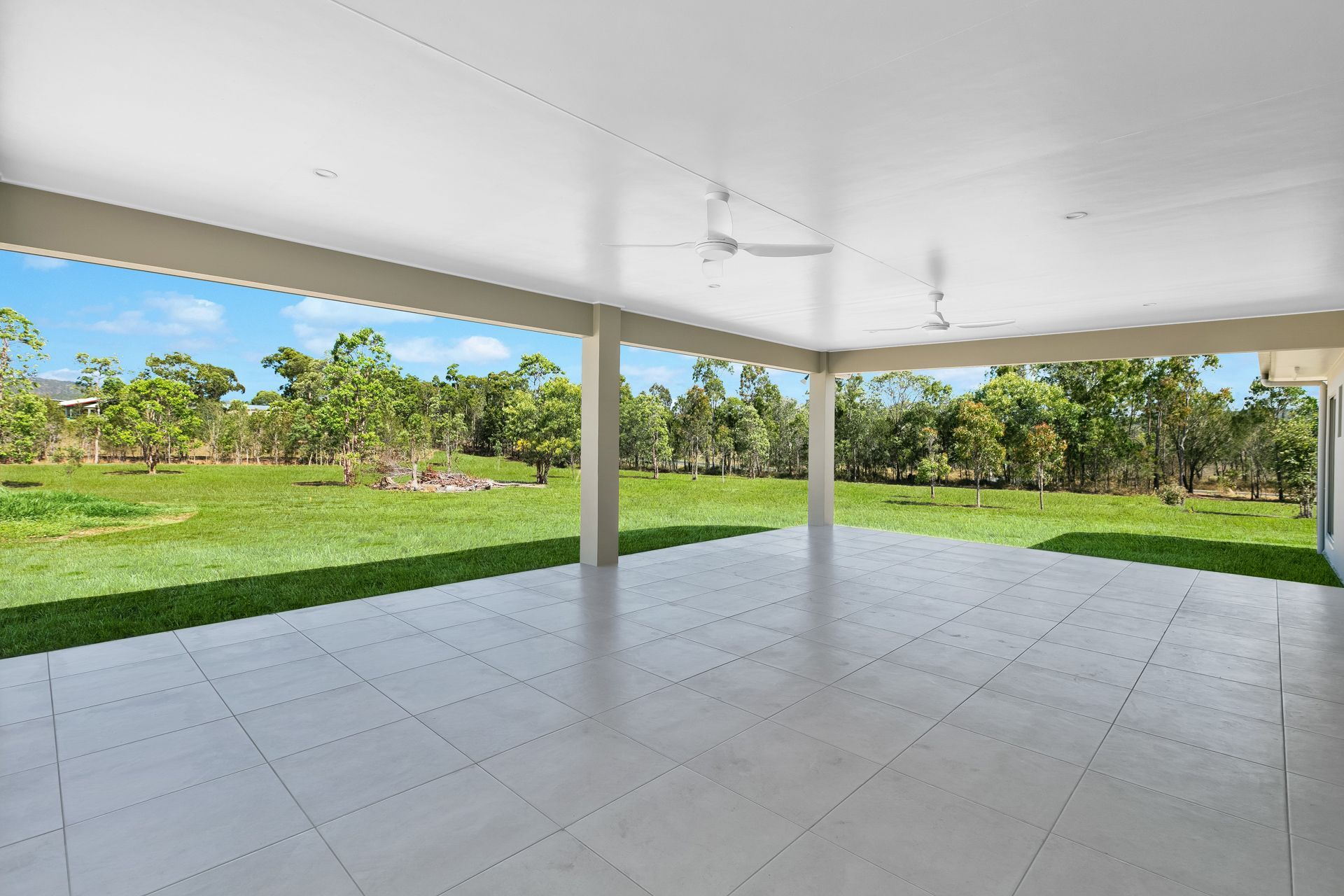 A Spacious, Covered Outdoor Patio With Light Grey Tiled Flooring — Ashlee Jones Homes in Gordonvale, QLD