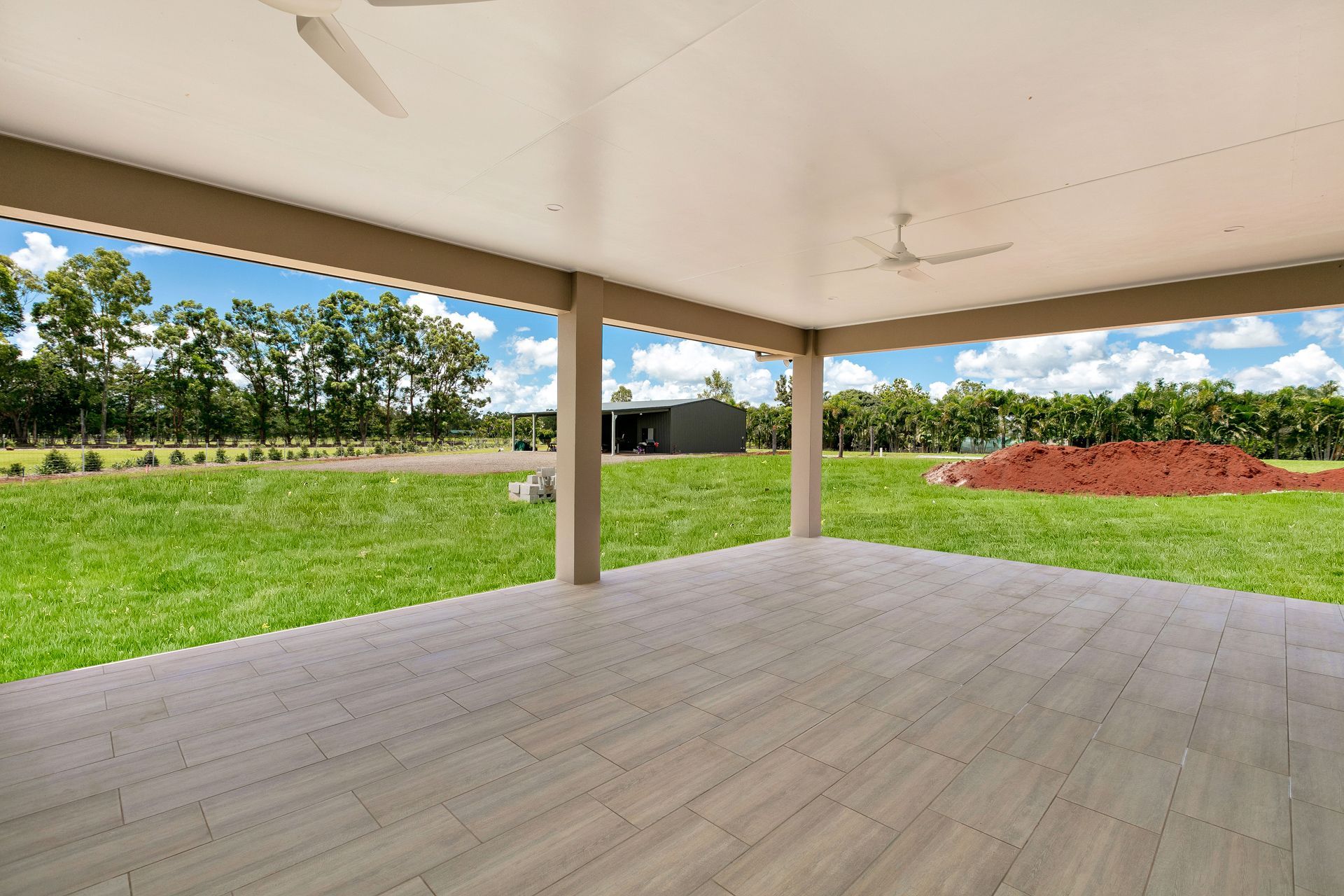 A Covered Tiled Patio Looking Out Onto a Grassy Yard — Ashlee Jones Homes in Gordonvale, QLD