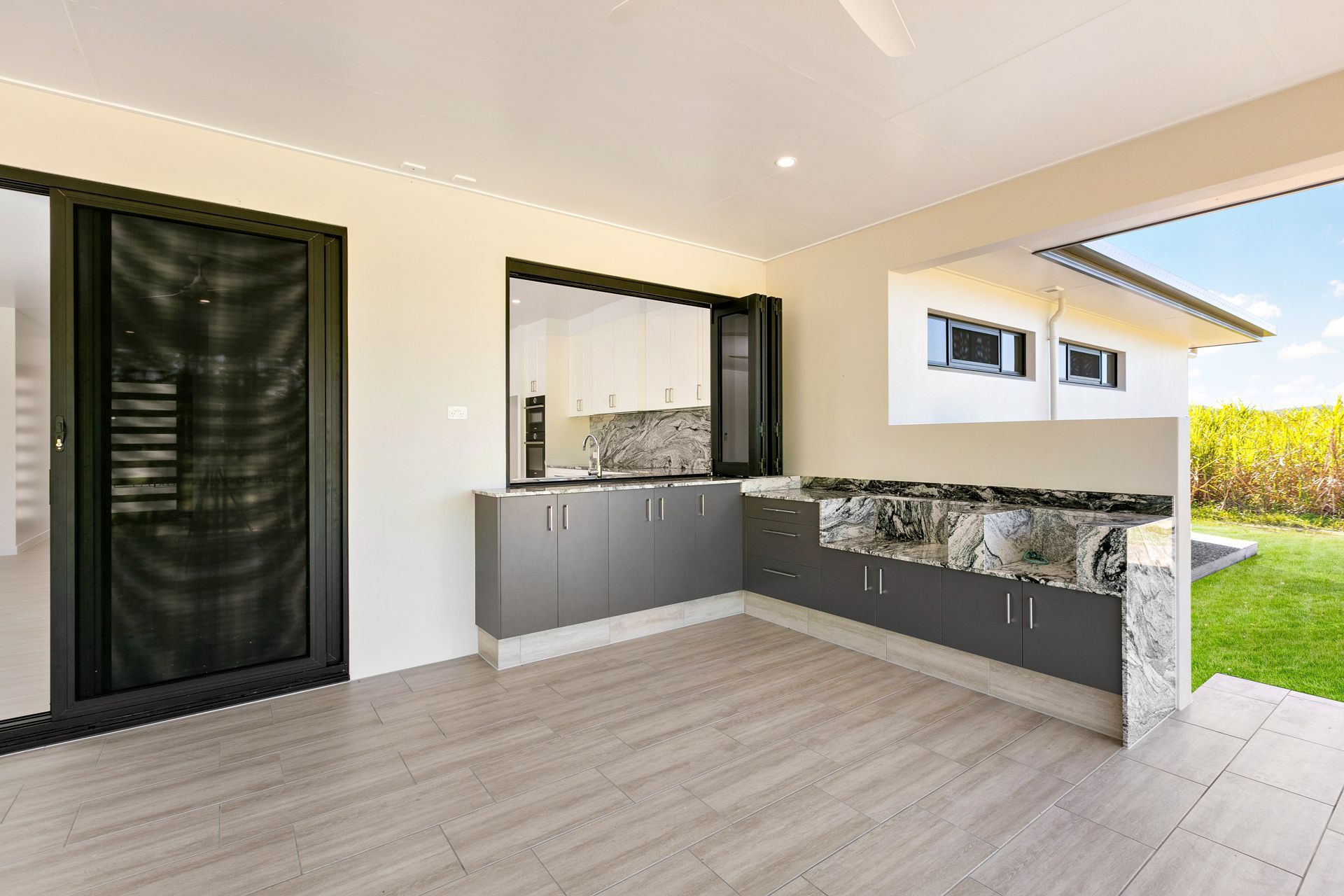 An Outdoor Kitchen Area With Grey Cabinets and Marble Countertops — Ashlee Jones Homes in Gordonvale, QLD