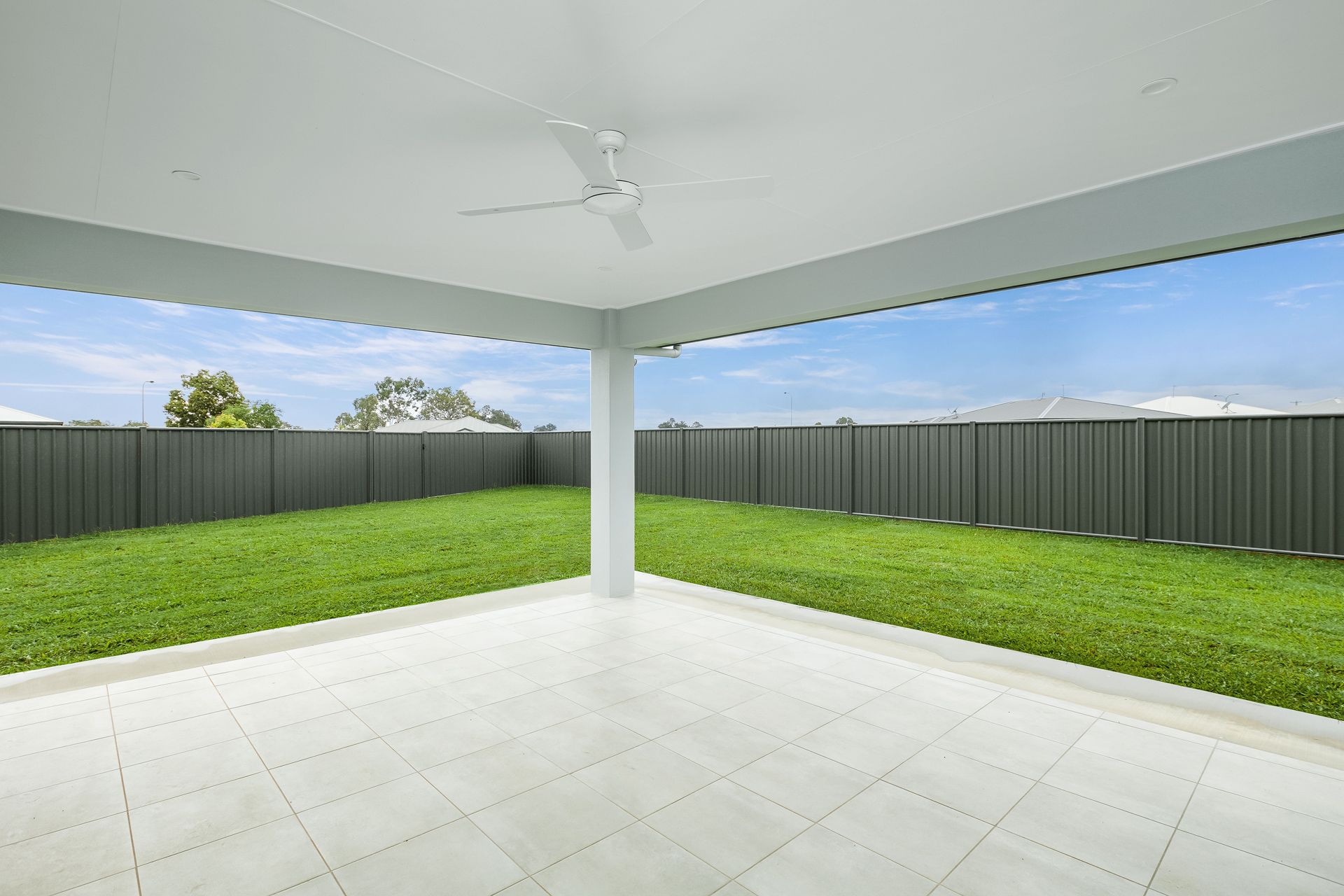 A Covered White Patio With a Ceiling Fan Overlooking a Lush Green Lawn — Ashlee Jones Homes in Gordonvale, QLD