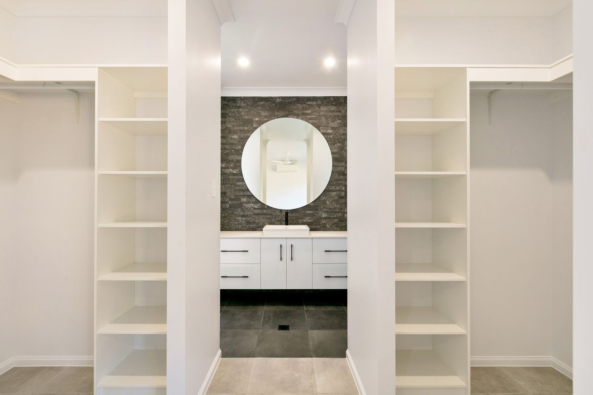 A Walk-through Wardrobe Leading to a Bathroom With a White Vanity — Ashlee Jones Homes in Gordonvale, QLD