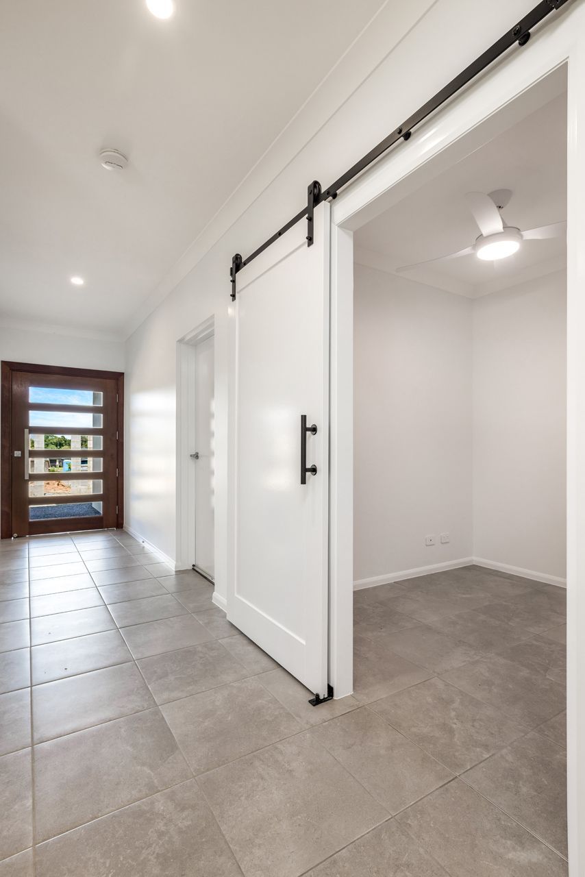 A Bright Hallway With Gray Tiled Floors, a White Sliding Barn Door — Ashlee Jones Homes in Gordonvale, QLD