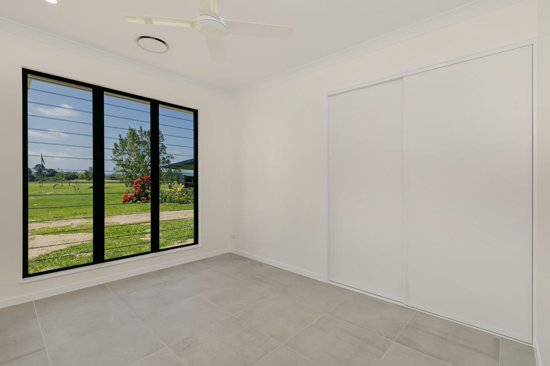 A Minimalist Bedroom With White Walls, Light Gray Tile Floors — Ashlee Jones Homes in Gordonvale, QLD