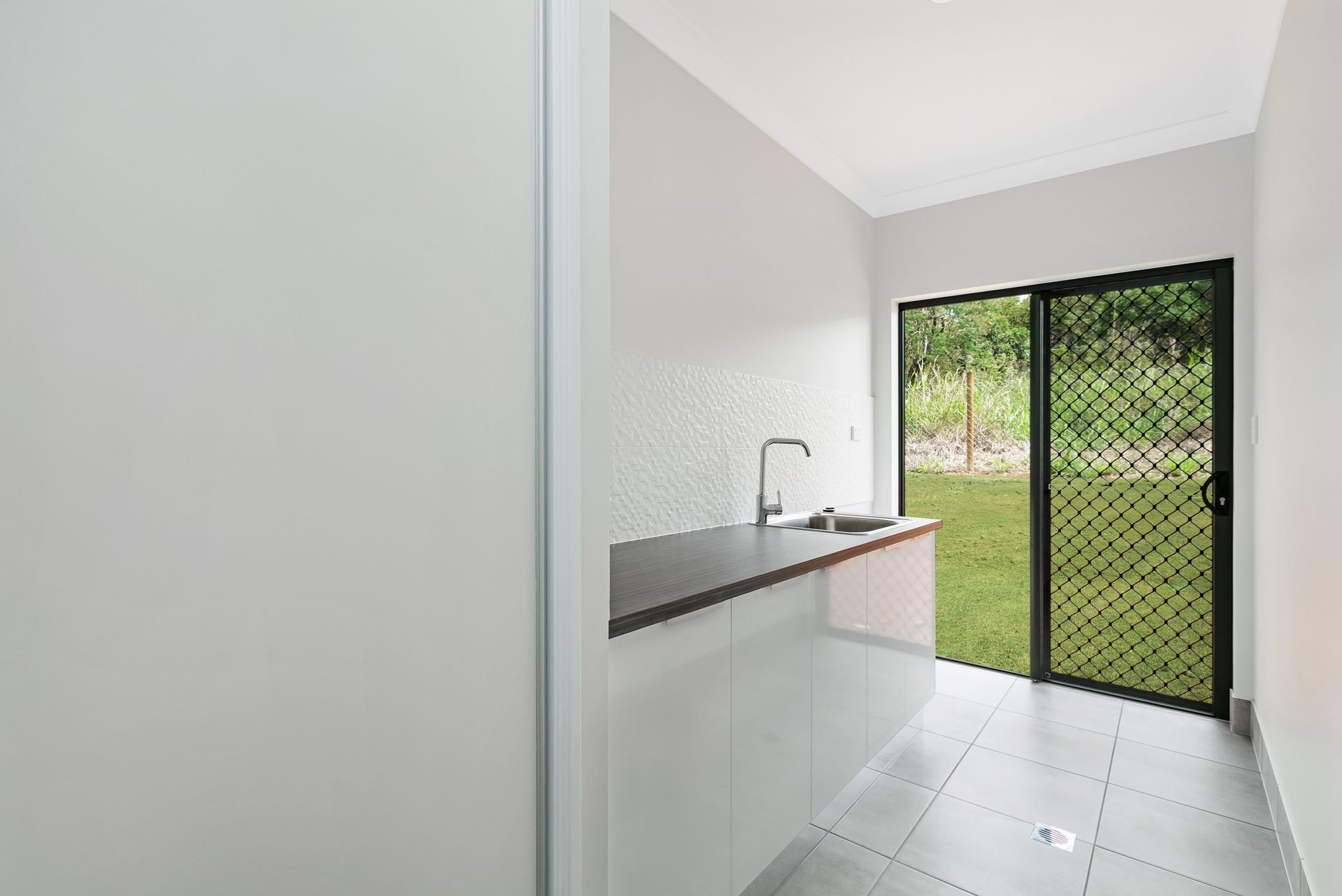 A Bright Laundry or Utility Room With a White Cabinet, Dark Countertop — Ashlee Jones Homes in Gordonvale, QLD
