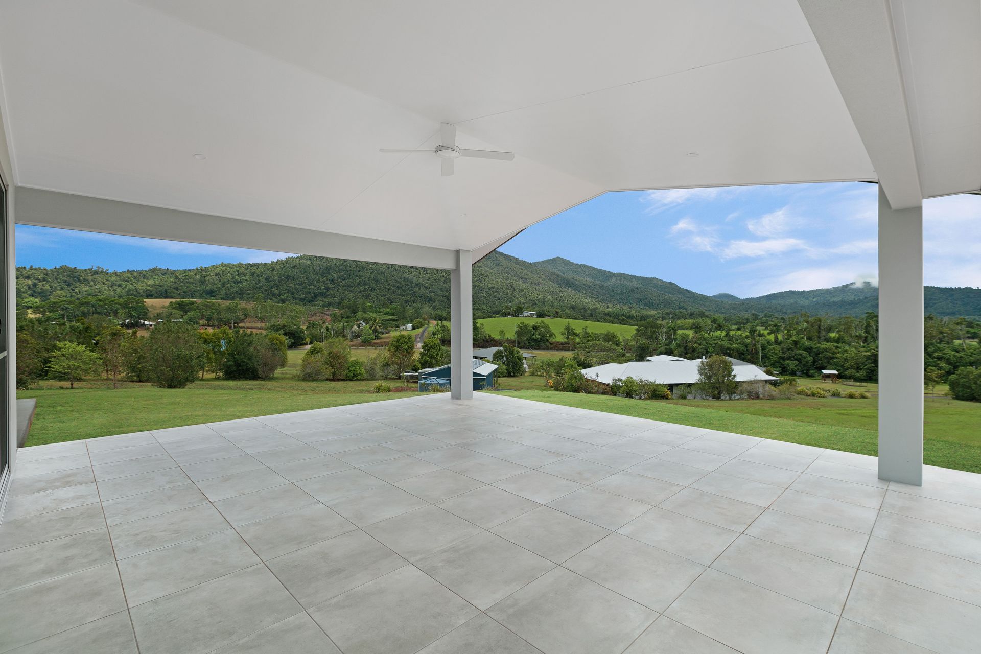 A Spacious, Light-grey Tiled Patio Under a White Roof Looks Out Over a Lush Green — Ashlee Jones Homes in Gordonvale, QLD