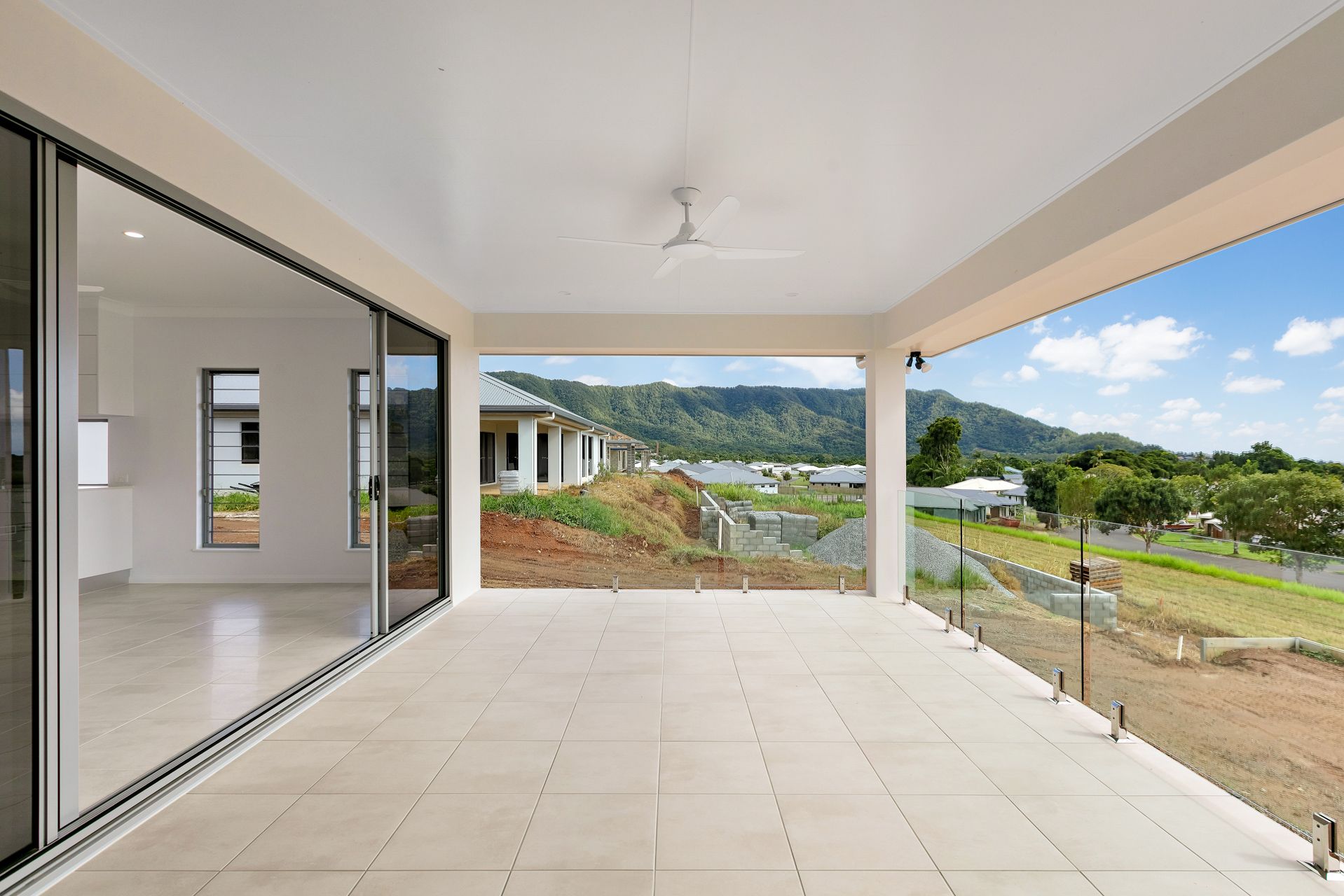 A Modern Covered Patio With Light Tiles and a Glass Railing — Ashlee Jones Homes in Gordonvale, QLD