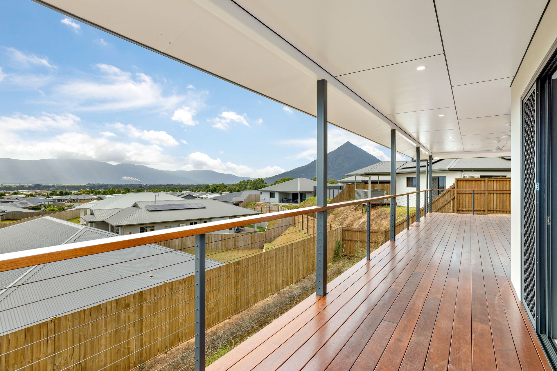 A Wooden Deck With a Modern Railing Overlooking a Residential Neighborhood — Ashlee Jones Homes in Gordonvale, QLD