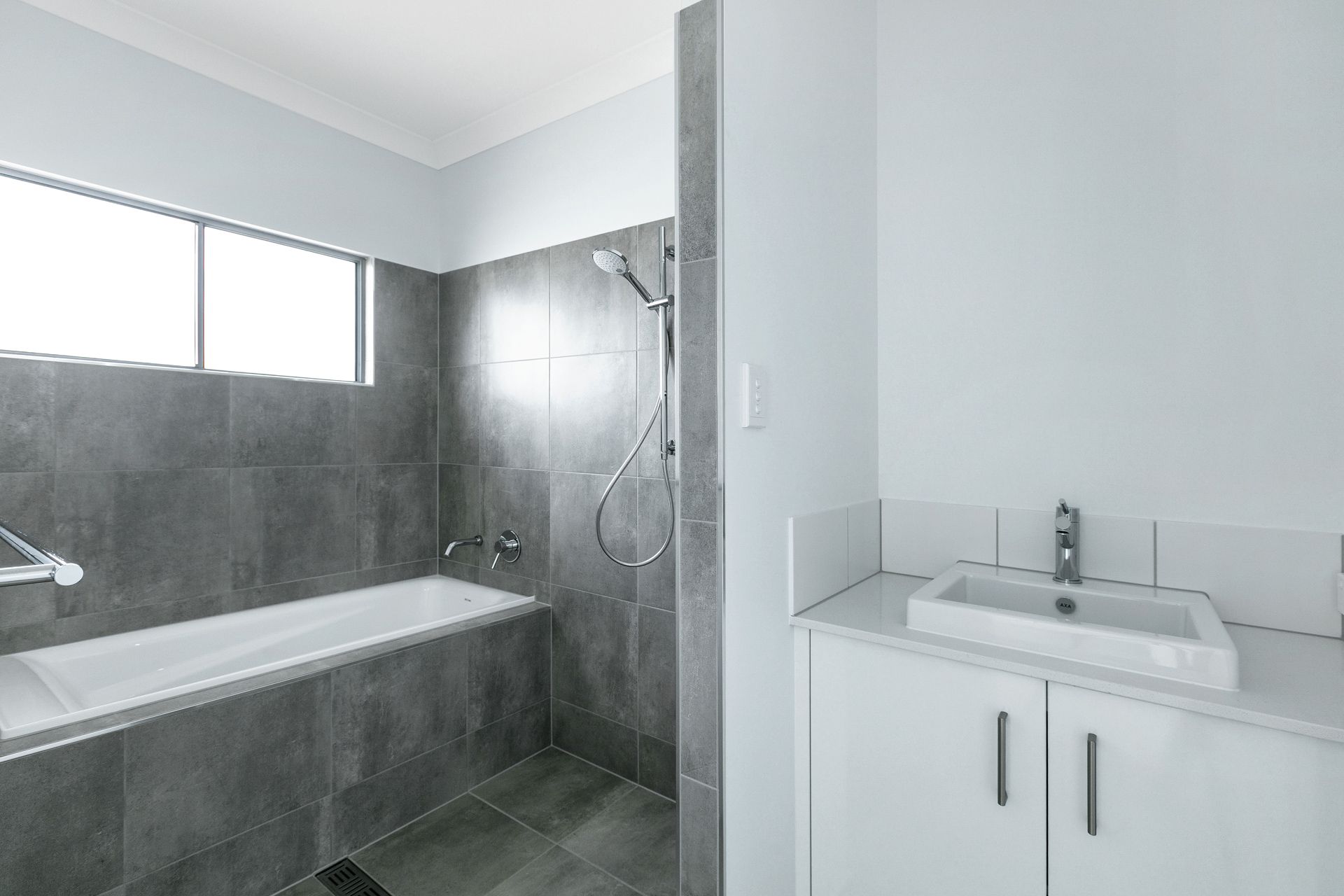 A Modern Bathroom With a Grey Tiled Bathtub Area — Ashlee Jones Homes in Gordonvale, QLD