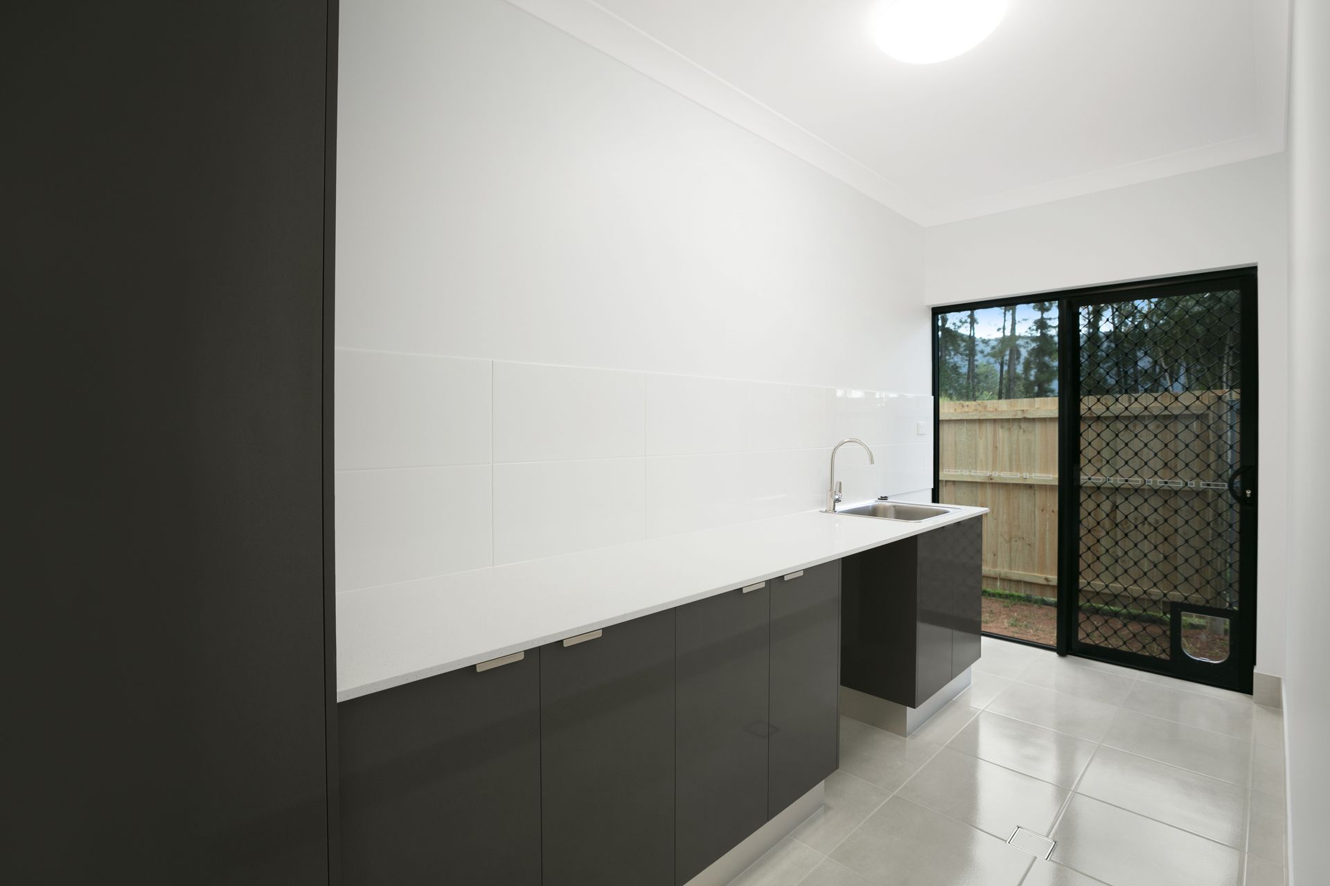 Modern Laundry Room With White Walls, Dark Gray Cabinetry — Ashlee Jones Homes in Gordonvale, QLD