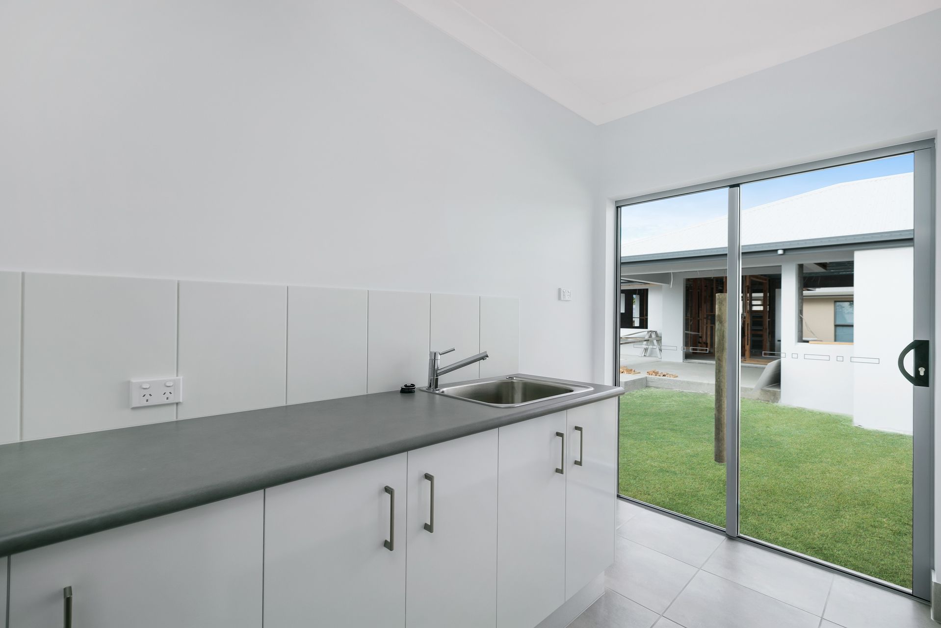 A White Kitchen Cabinet With a Dark Countertop and Sink — Ashlee Jones Homes in Gordonvale, QLD