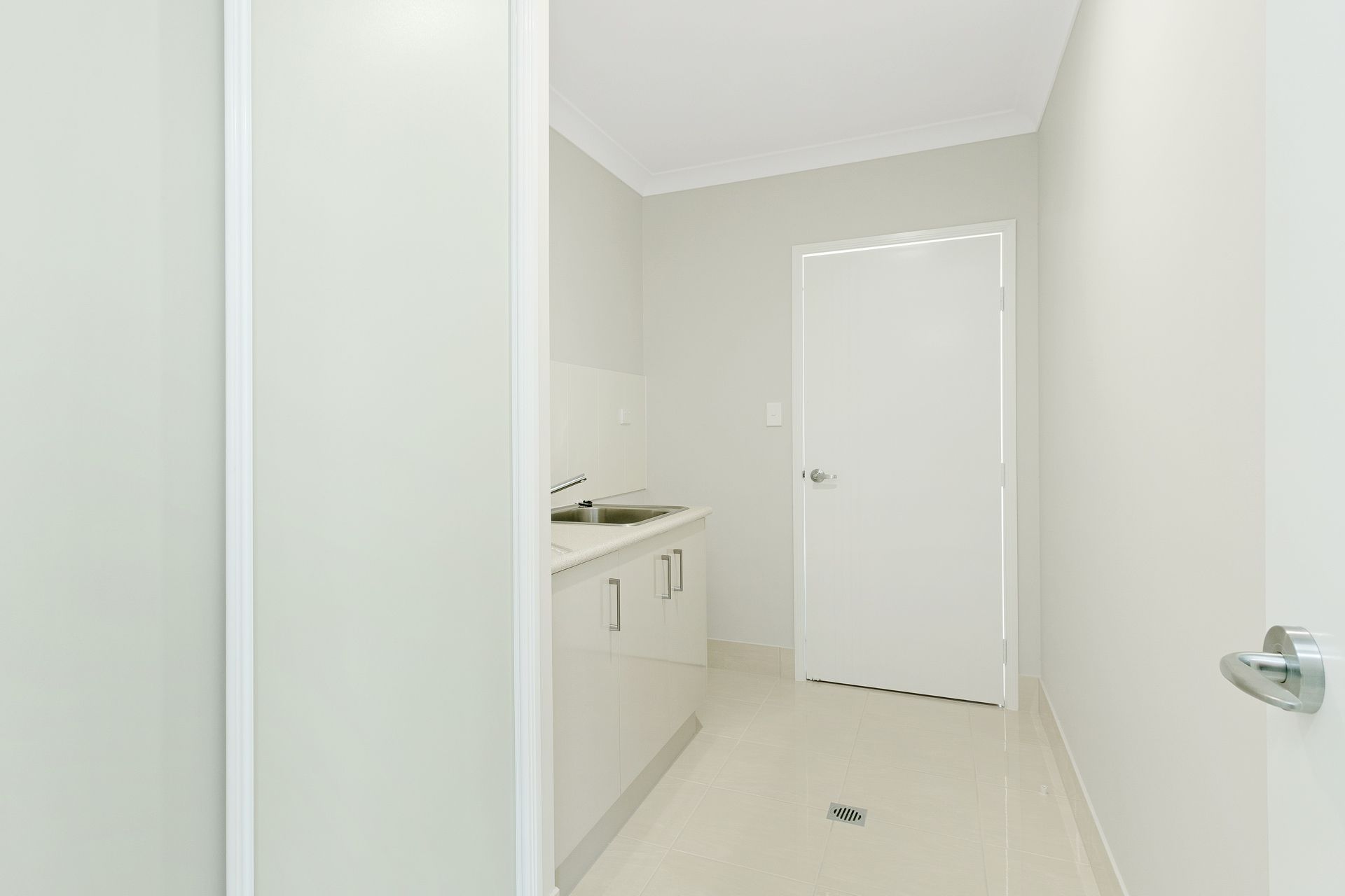 A Laundry Room With Off-white Walls, White Cabinets With a Metal Sink — Ashlee Jones Homes in Gordonvale, QLD