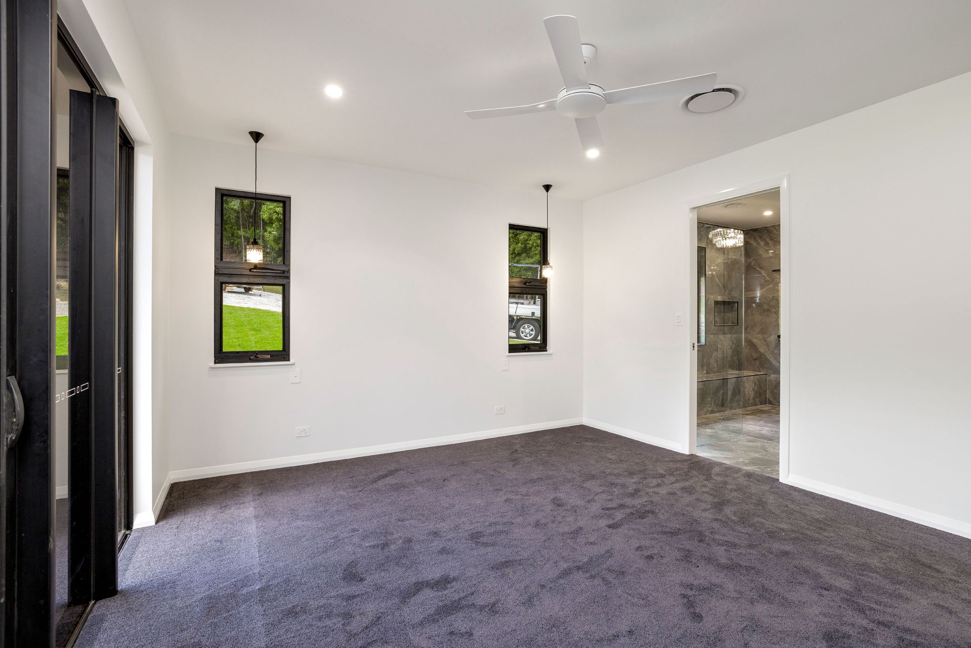 A Bright, Empty Bedroom With White Walls, Dark Gray Carpet — Ashlee Jones Homes in Gordonvale, QLD