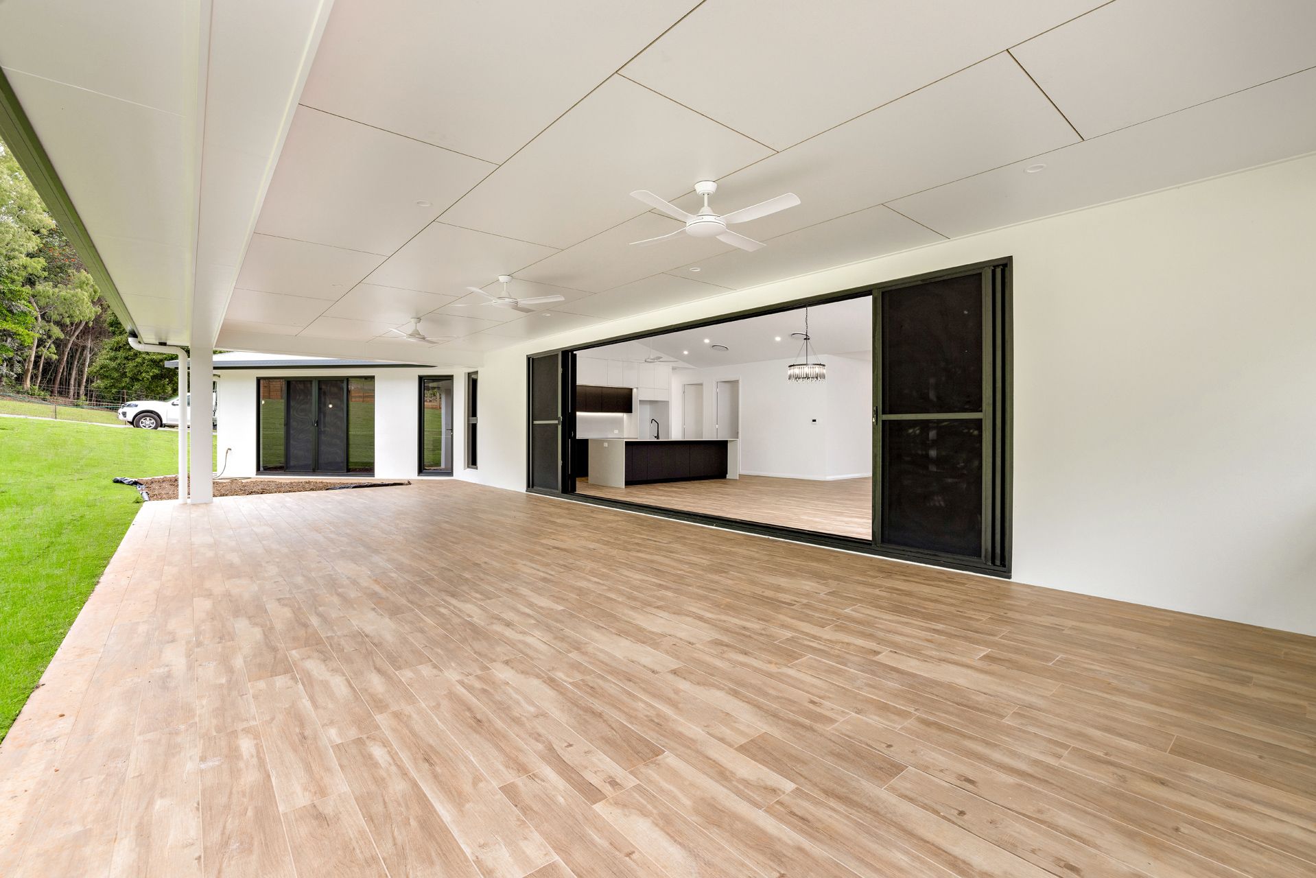 A Wide, Covered Patio With Light Wood-look Flooring Overlooks a Green Lawn — Ashlee Jones Homes in Gordonvale, QLD