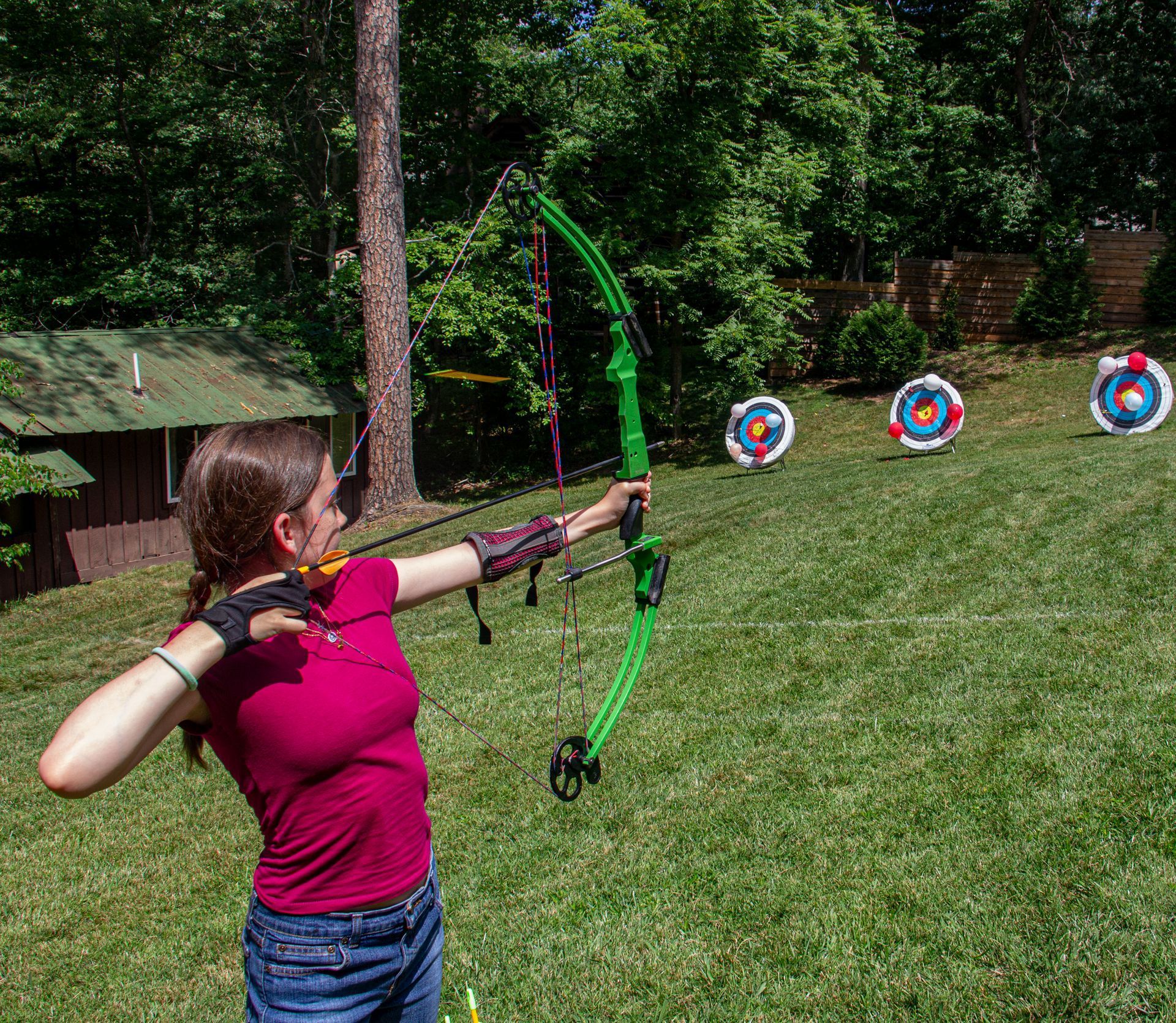 Two green archery bow stands holding clusters of arrows with orange fletching in a grassy field.