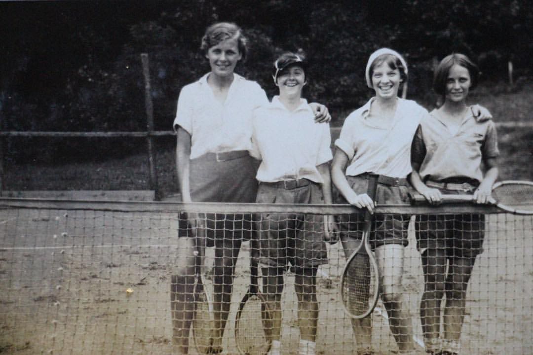 Four people standing behind a tennis net holding rackets on an outdoor court