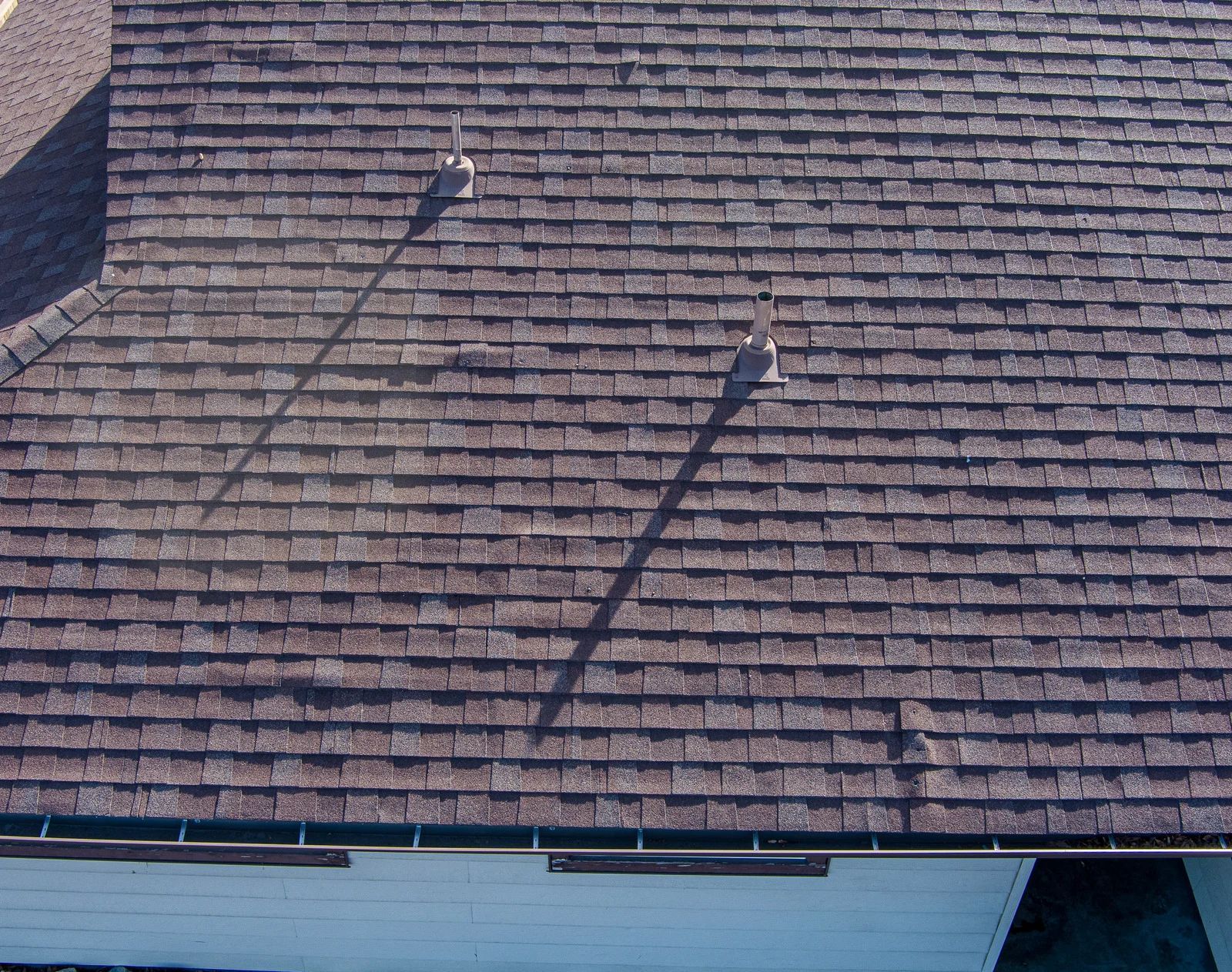 Brown shingled roof with two vents and long shadows in sunlight