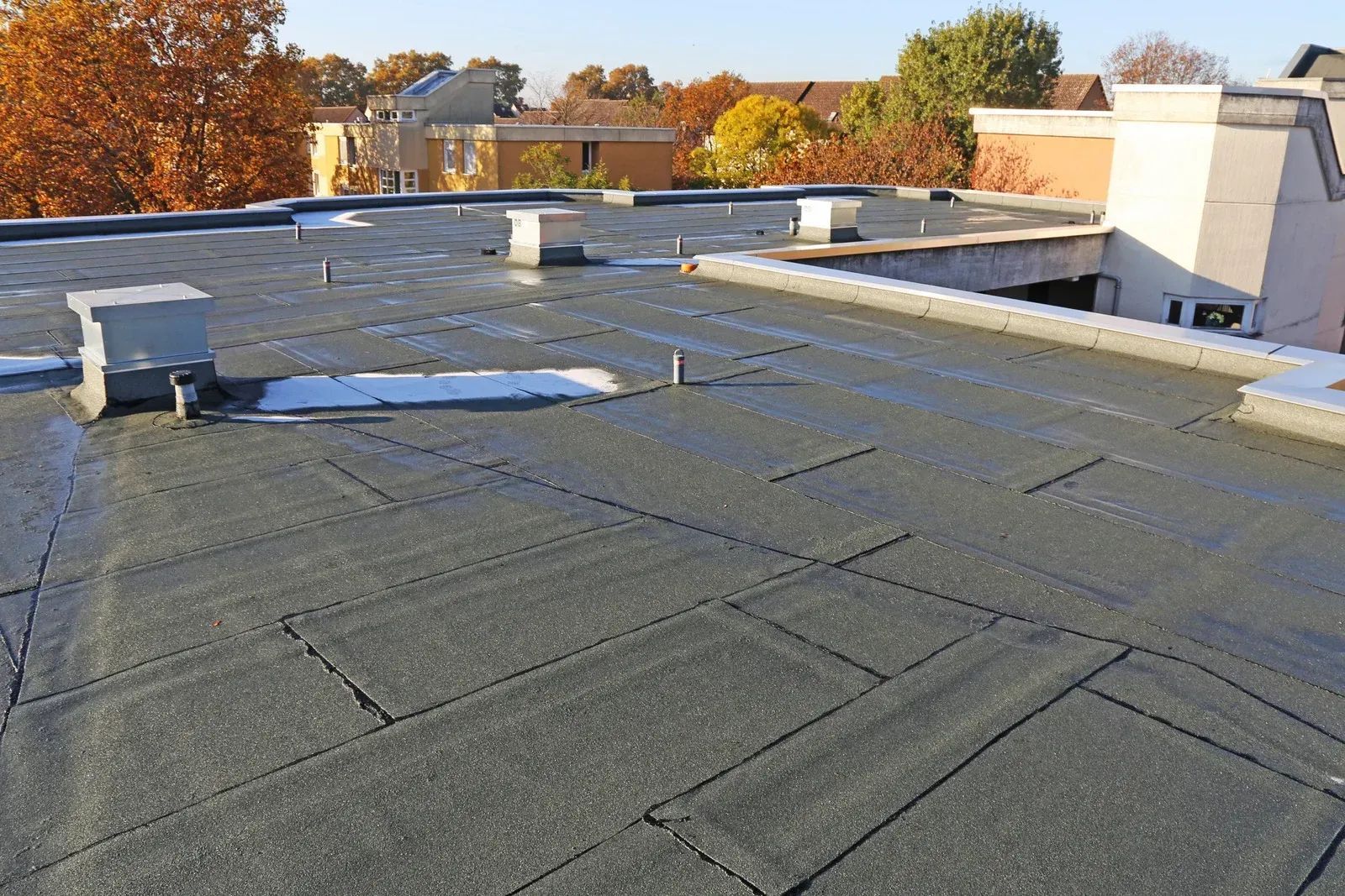 Flat commercial rooftop with vents, gravel roofing, and autumn trees in the background