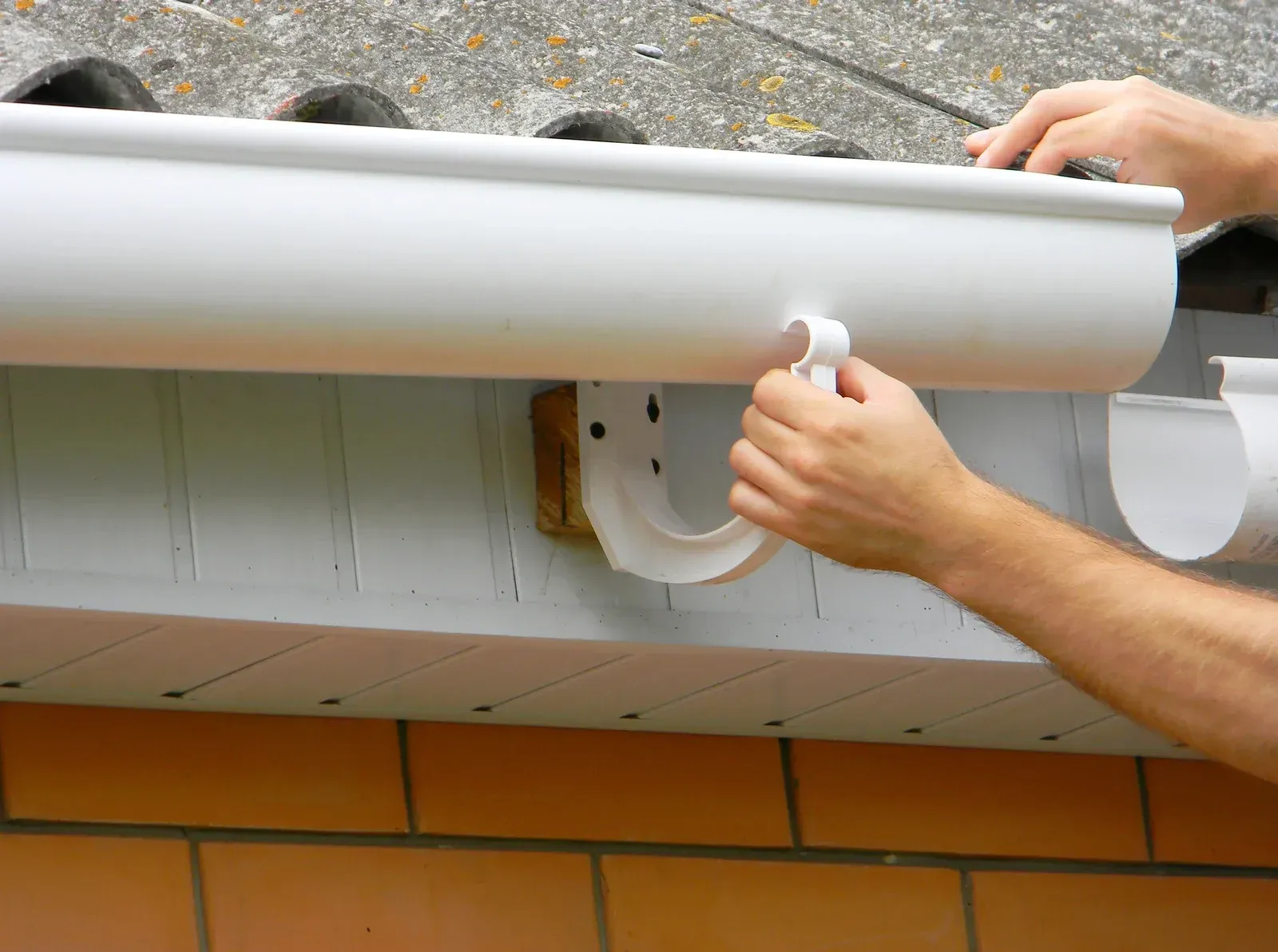 Hands installing a white rain gutter on a house exterior