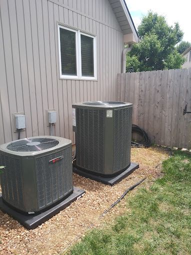 Two air conditioners are sitting outside of a house.