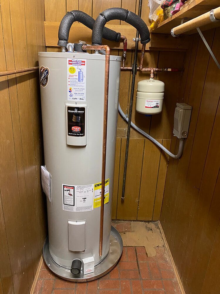 A water heater is sitting in a closet next to a wall.