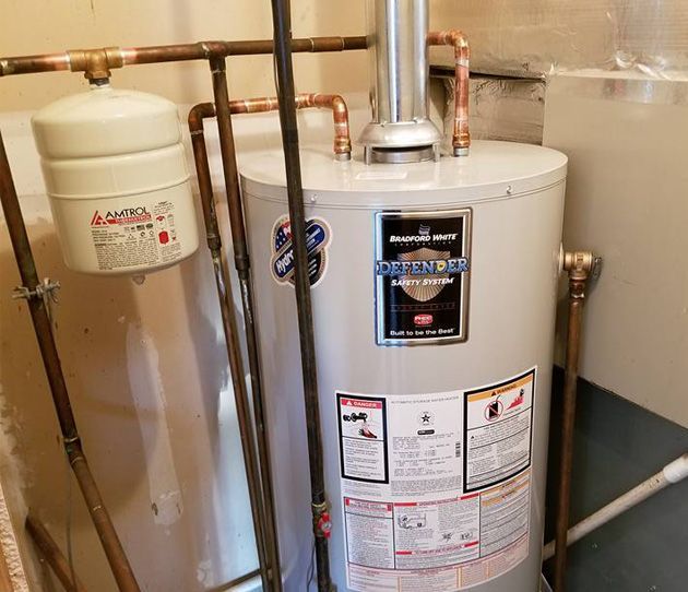 A water heater is sitting in a room next to a copper pipe.