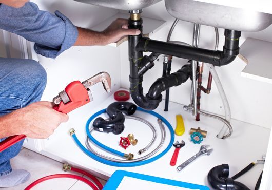 A plumber is fixing a sink with a wrench.