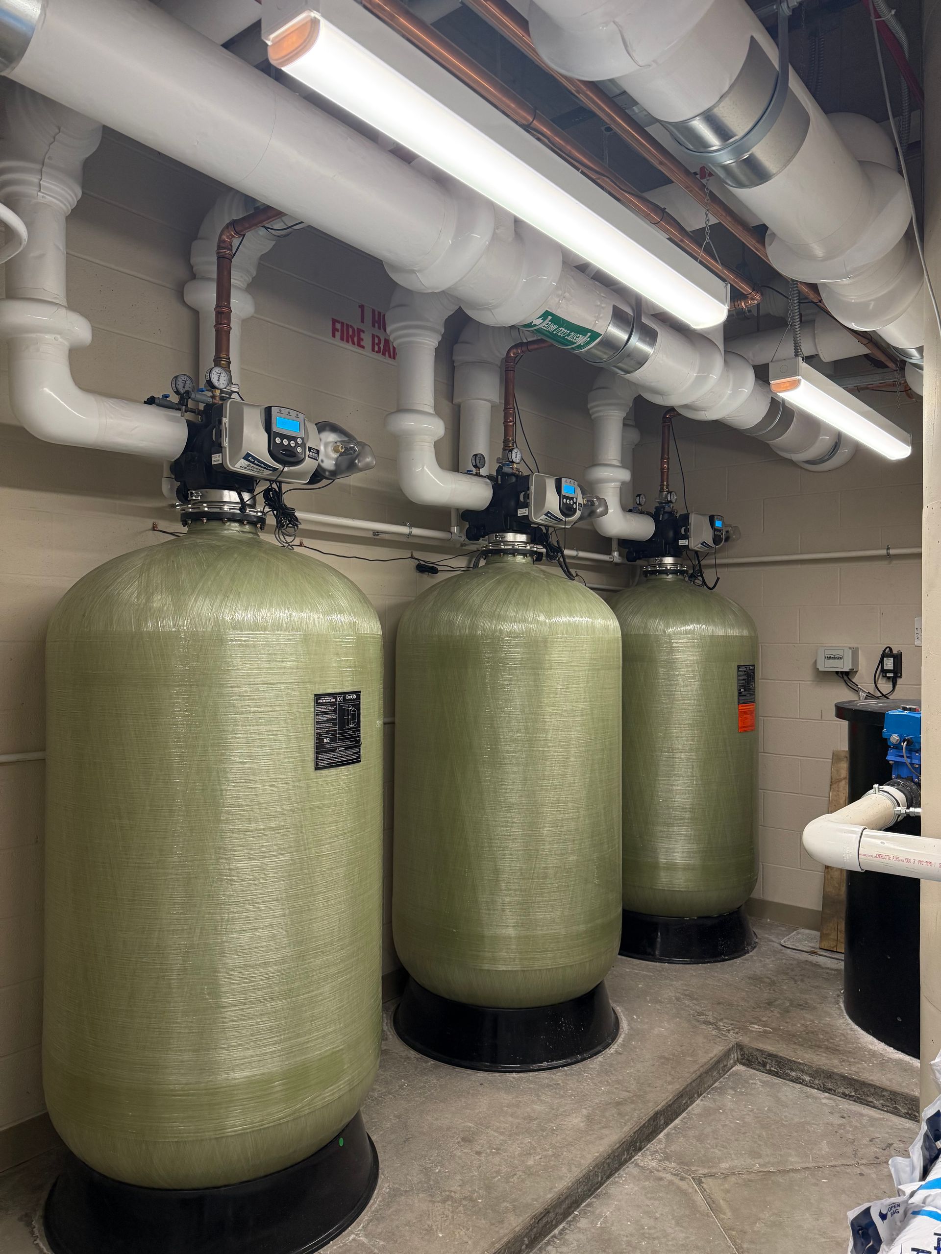 Three large cylindrical water filtration tanks with connected pipes in an industrial setting.