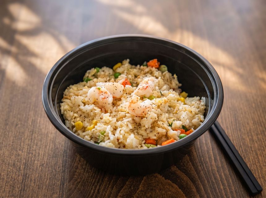 Bowl of fried rice with shrimp and vegetables, served on a wooden table with black chopsticks.