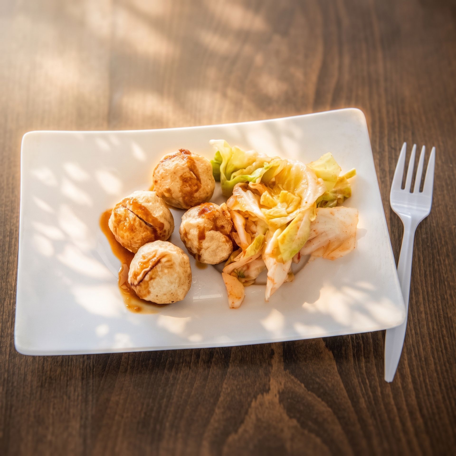 Plated meal of browned bites and salad on a white dish with a fork on a wooden table