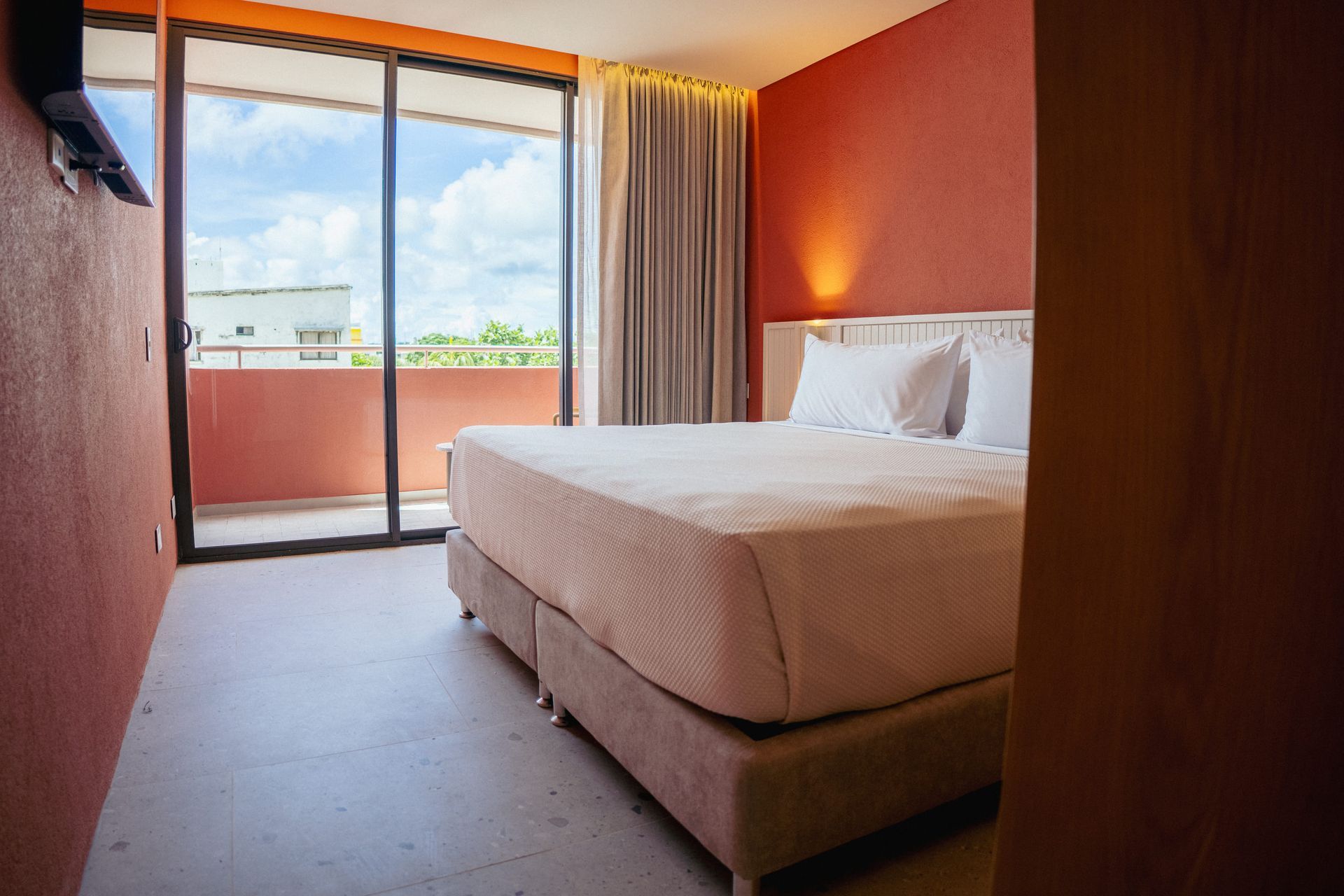 quartos em san andres com parede coral, cama king, cortinas claras e varanda com vista para o exterior.