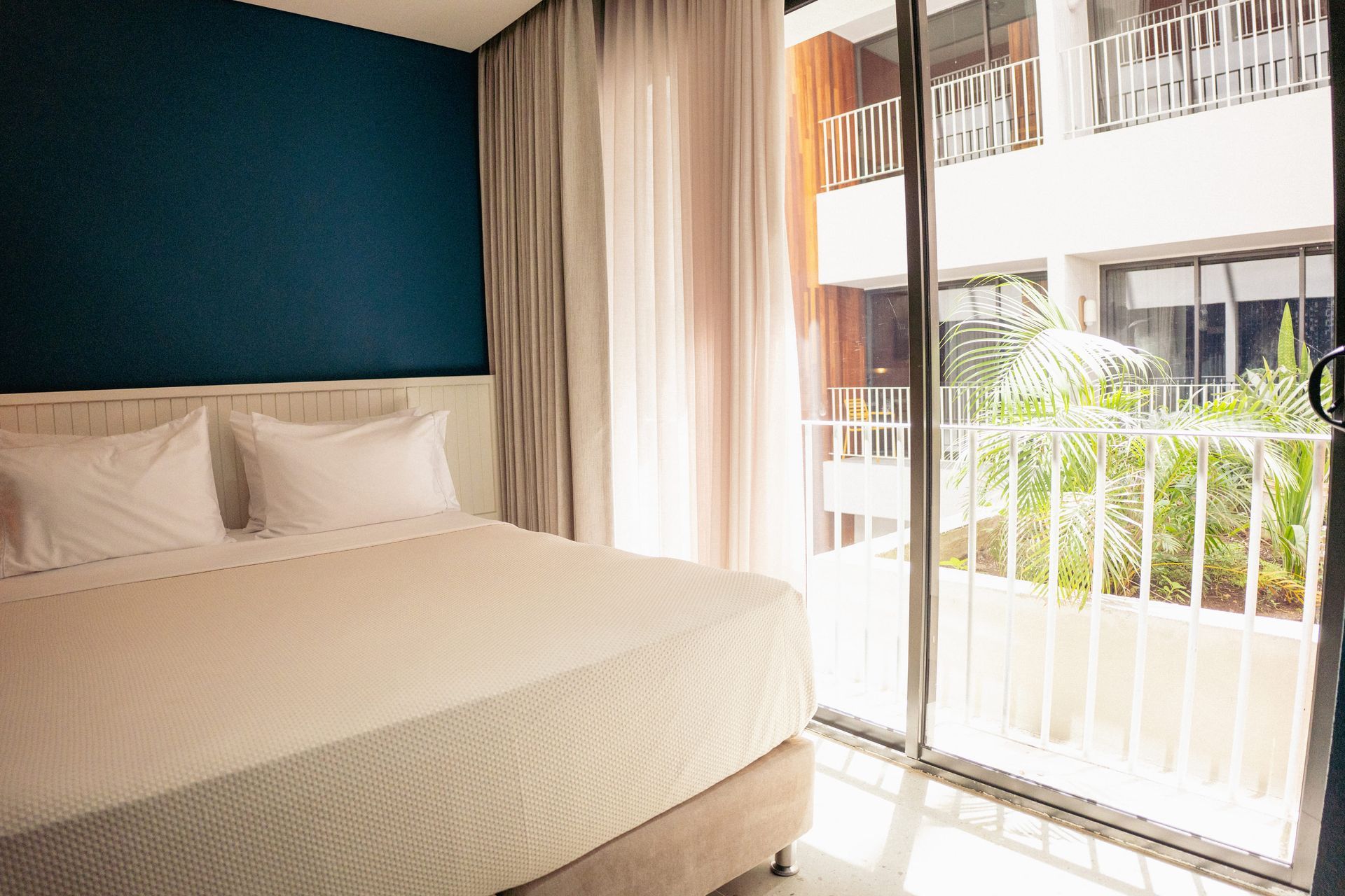 Hotel em San Andrés com quarto de cama ampla, parede azul, cortinas claras e varanda com grade branca.