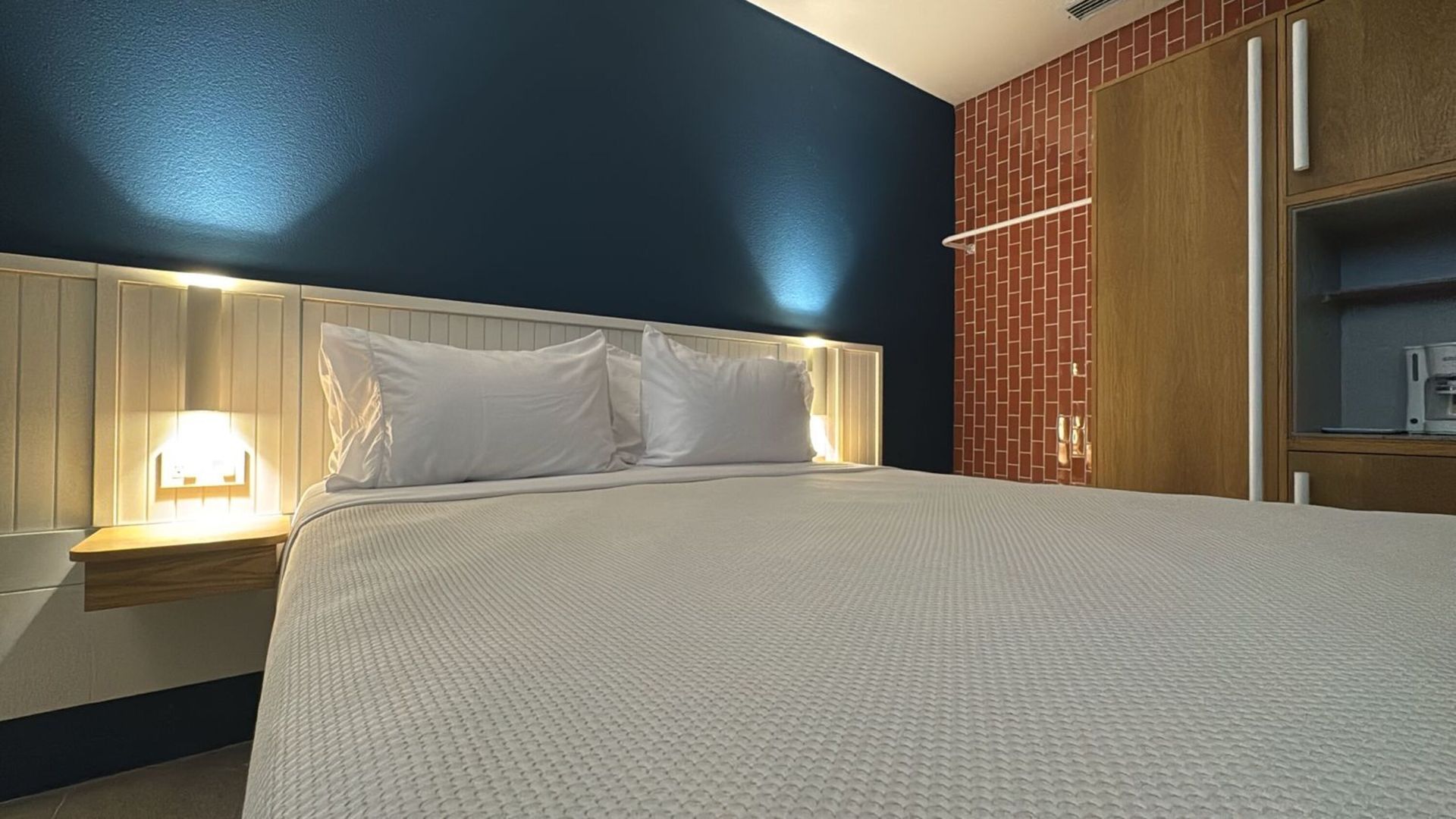 Quarto nas ilhas de San Andrés com cama queen, parede azul, cabeceira branca, luminária e parede coral.