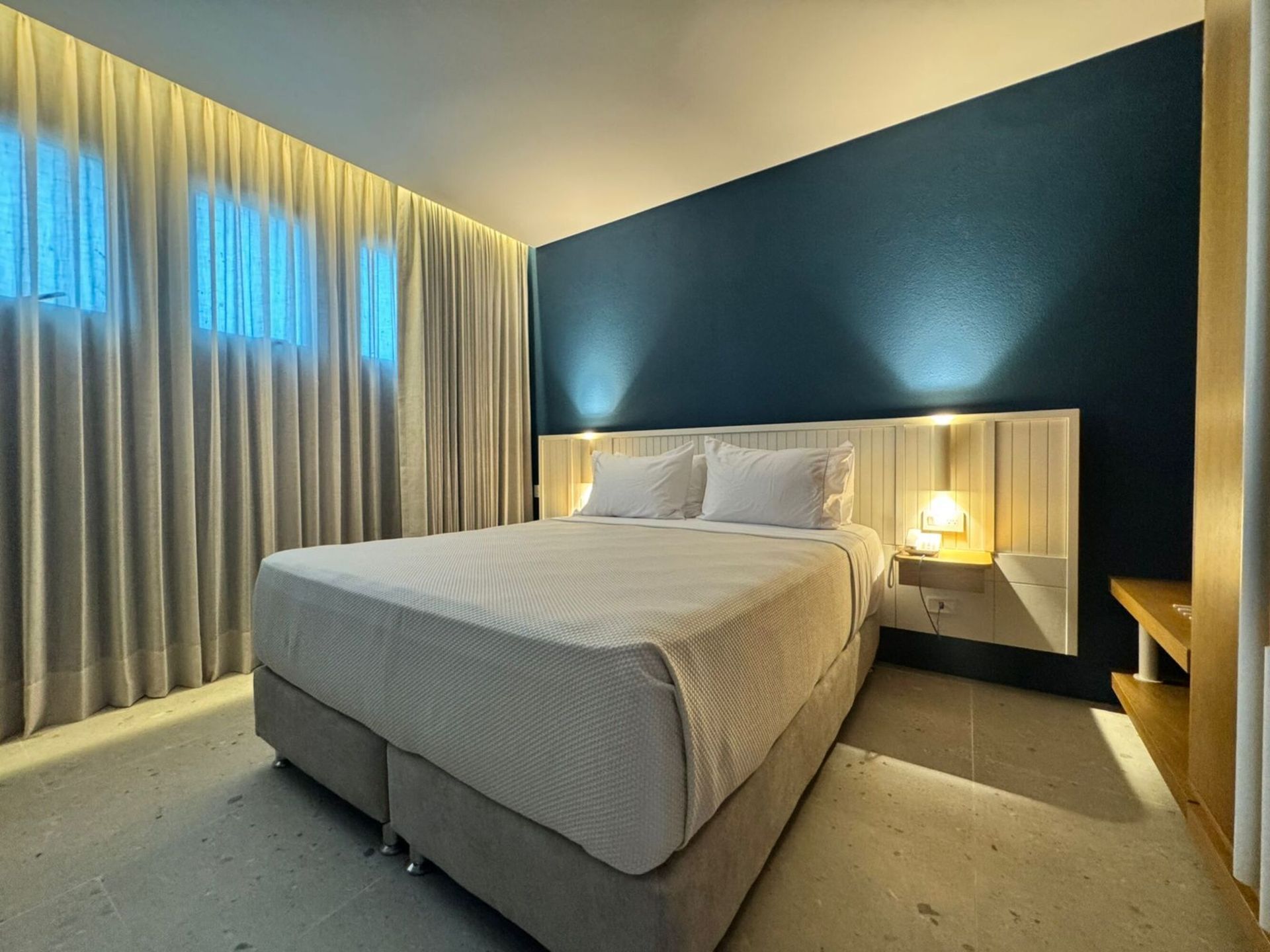 Hotel em San Andrés com quarto de cama queen, parede azul, cortinas cinzas e luz quente.