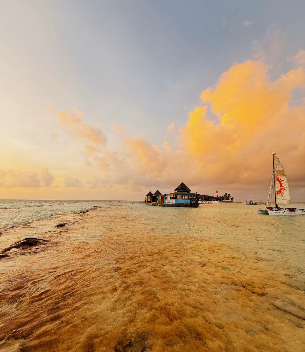Playa de San Andrés al atardecer con cielo dorado, mar tranquilo y velero junto al muelle.