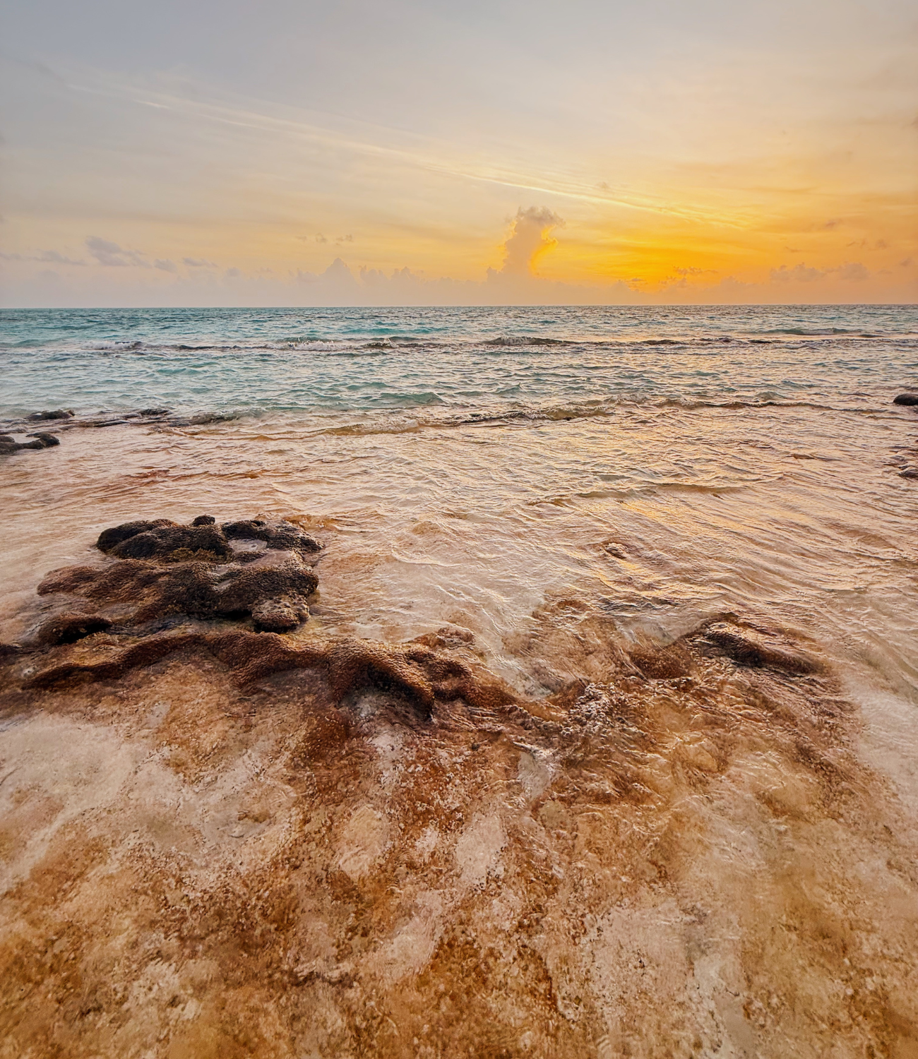 Olas suaves del mar de San Andrés sobre formaciones rocosas en la orilla, con agua cristalina y tonos dorados al atardecer.