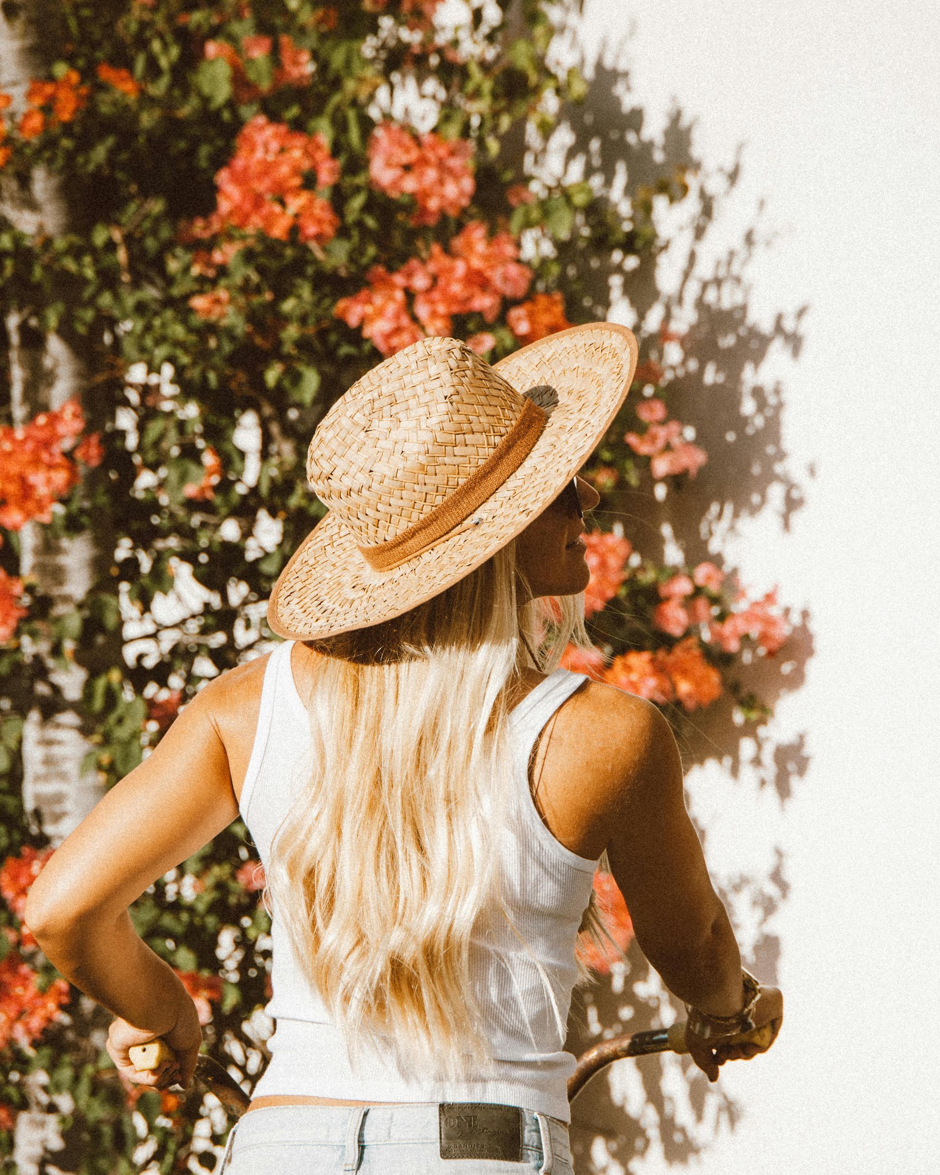 Mulher com chapéu em frente a uma árvore com flores.