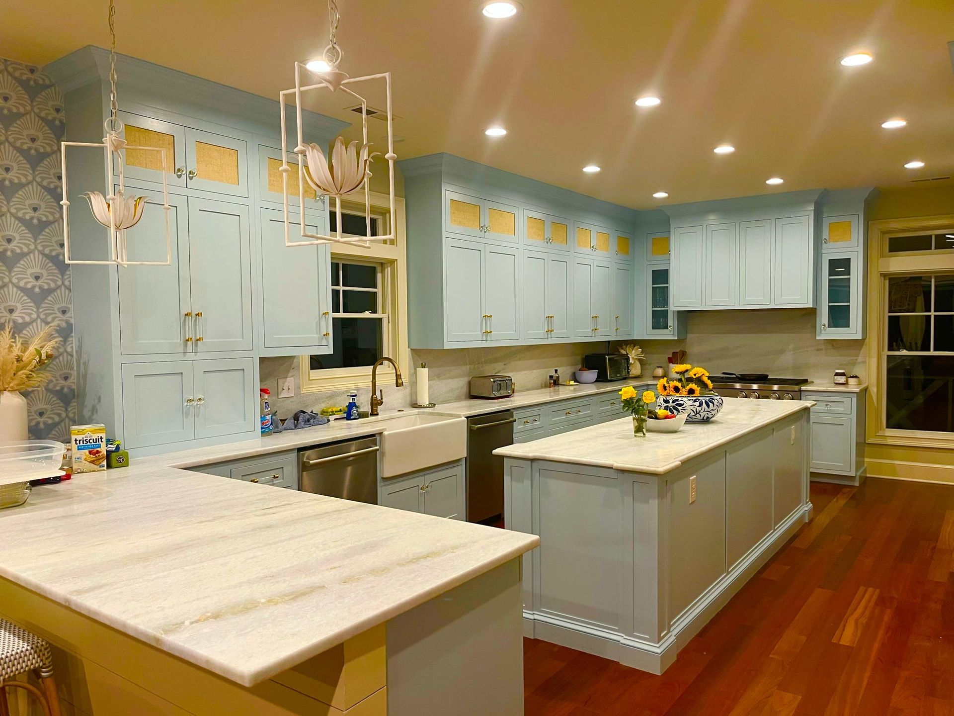 Spacious light-blue kitchen with white island, marble countertops, and warm wood floors.