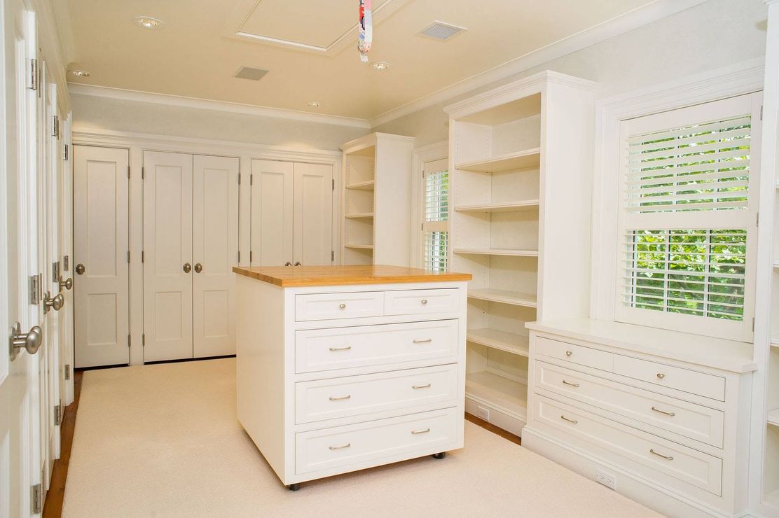 Bright white walk-in closet with built-in shelves, drawers, and a central island with a wood top.