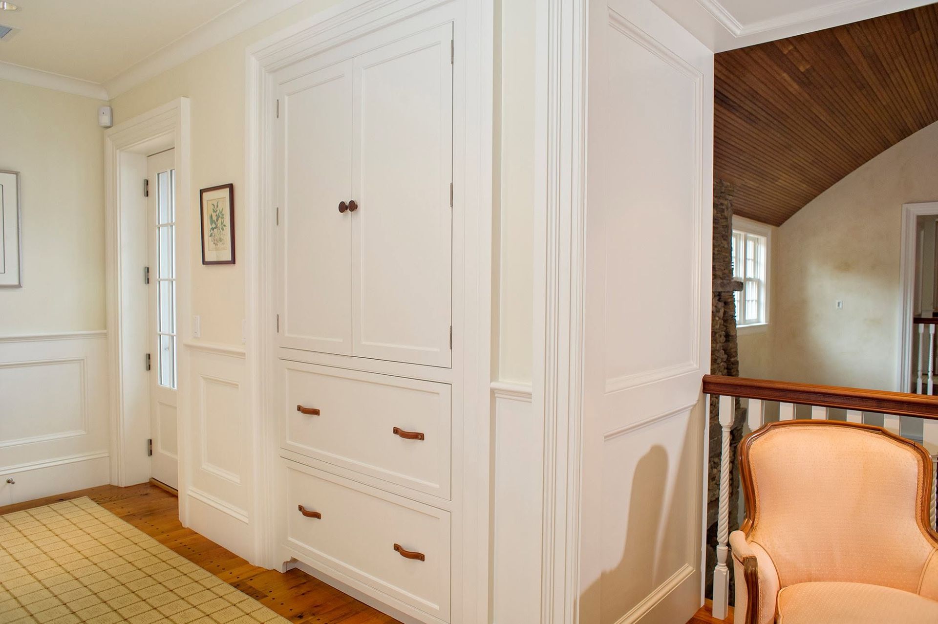 Bright hallway with built-in white cabinets, wood floor, and a peach armchair near an archway