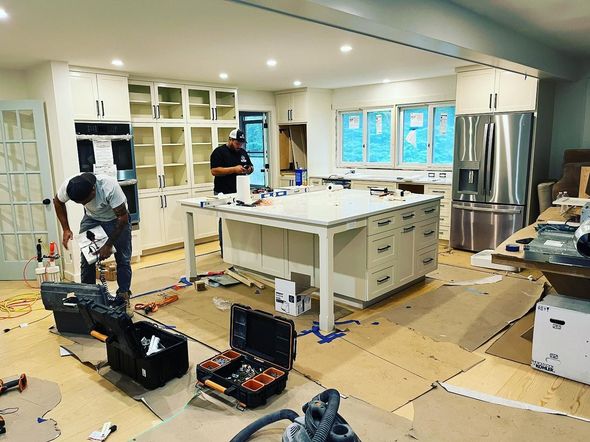 Kitchen under renovation with workers, tools, and floor protection around a central island