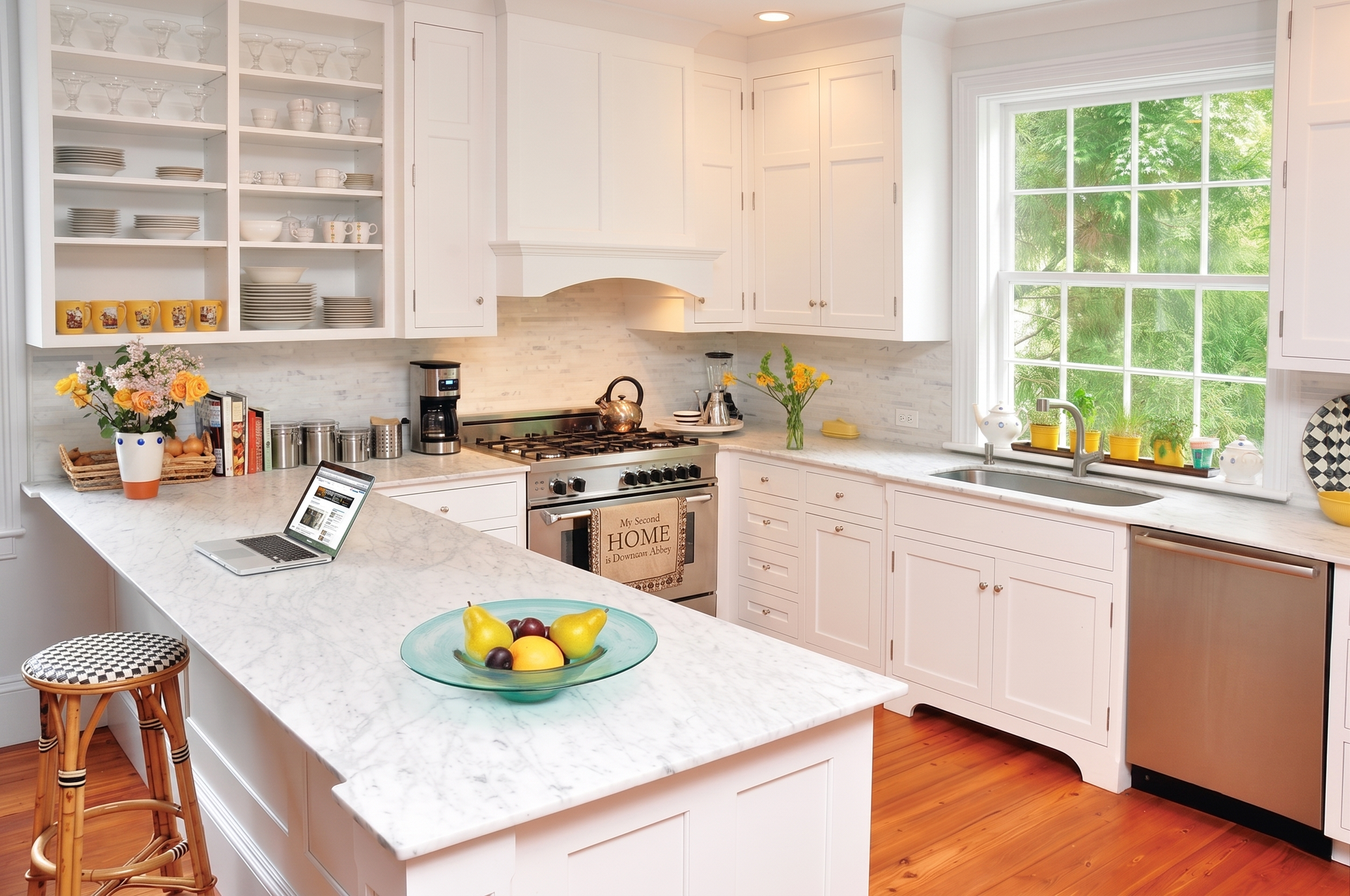 Bright white kitchen with marble island, stainless appliances, and a large window over the sink.